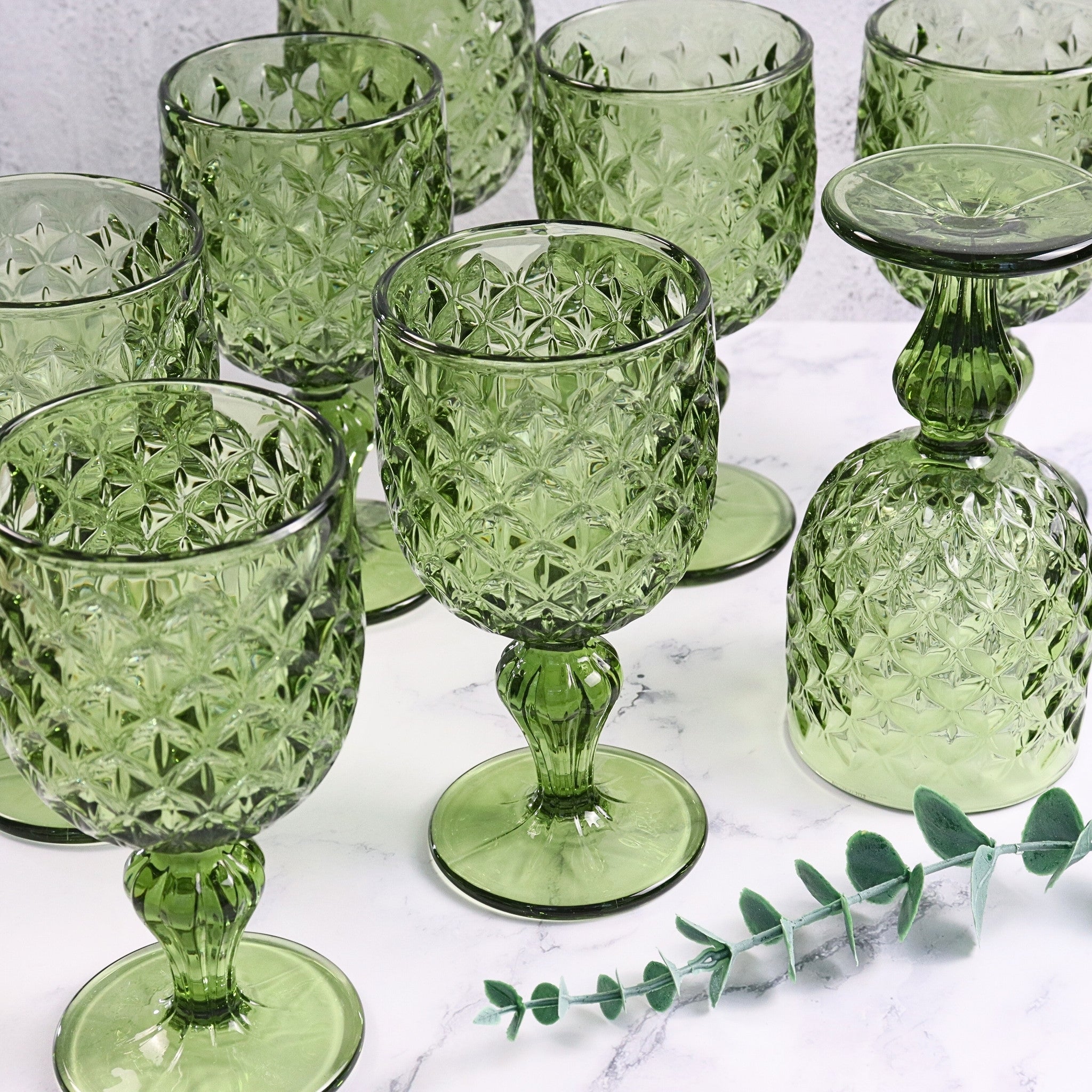 Set of green glass goblets on a marble surface with a small leaf decoration.