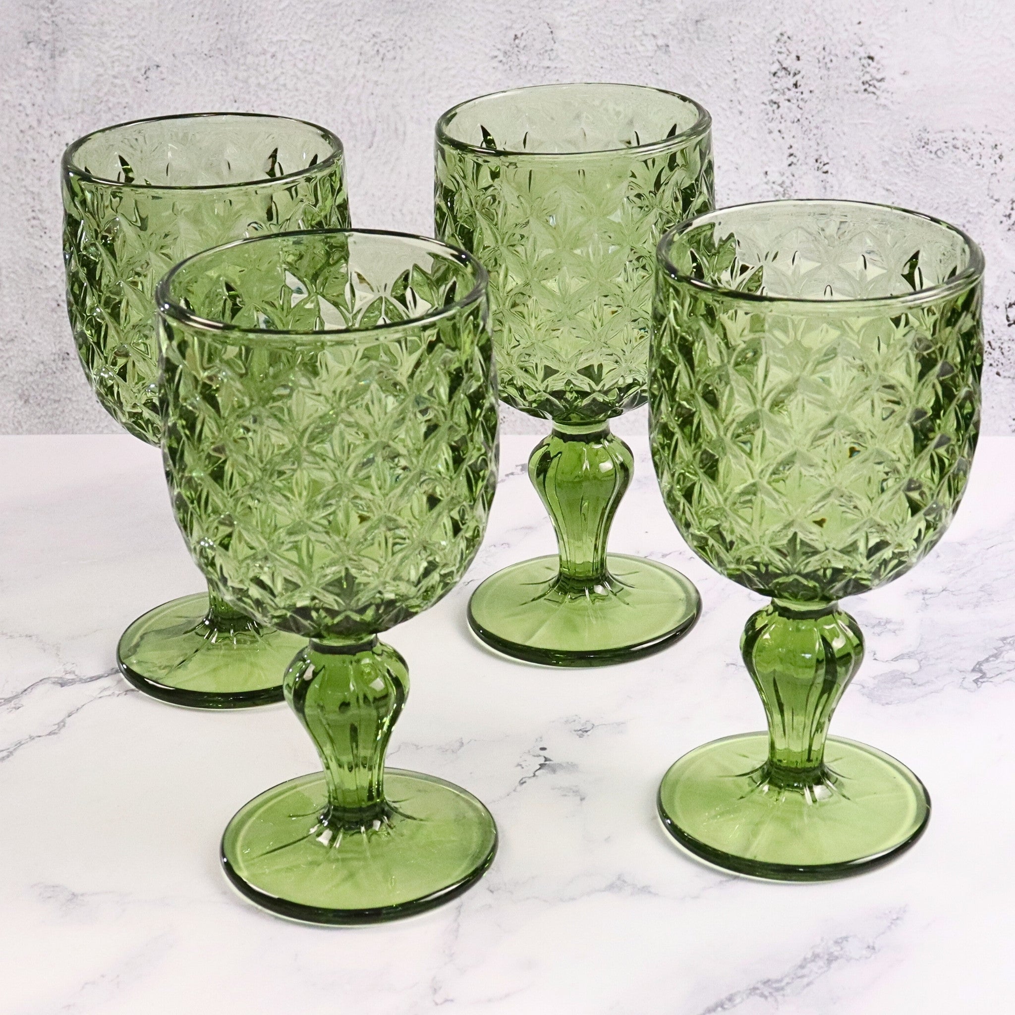 Set of four green glass goblets with textured design on a marble surface.
