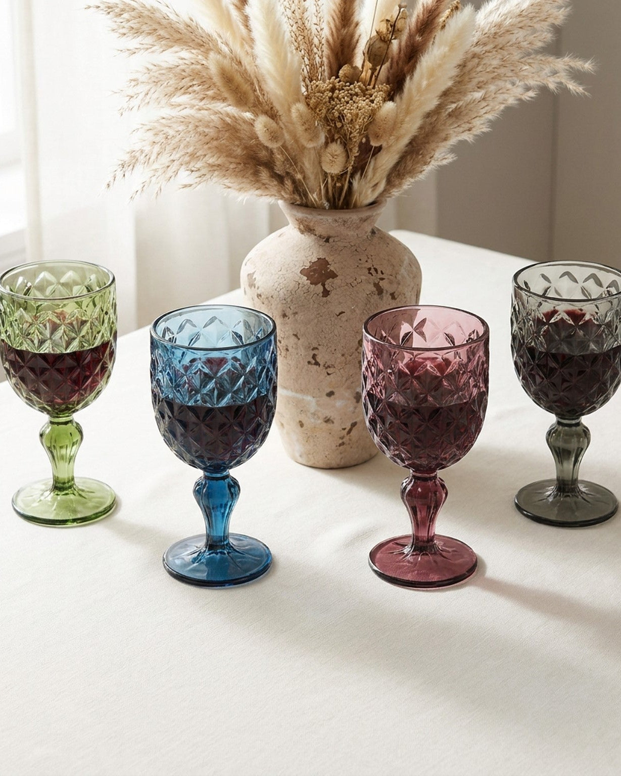 Four colorful glass goblets with textured designs on a marble surface.
