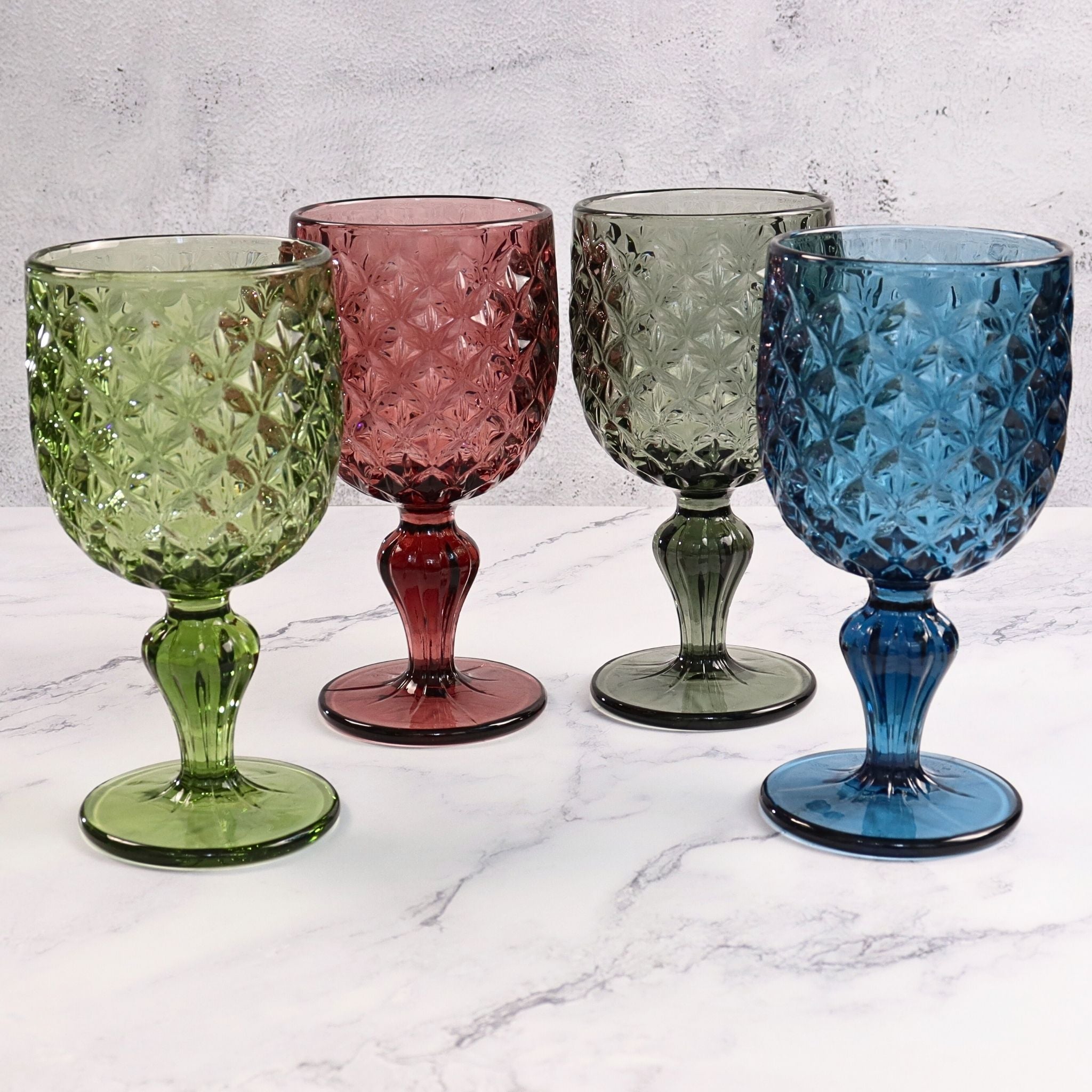 Four colorful glass goblets on a marble surface with a light gray background