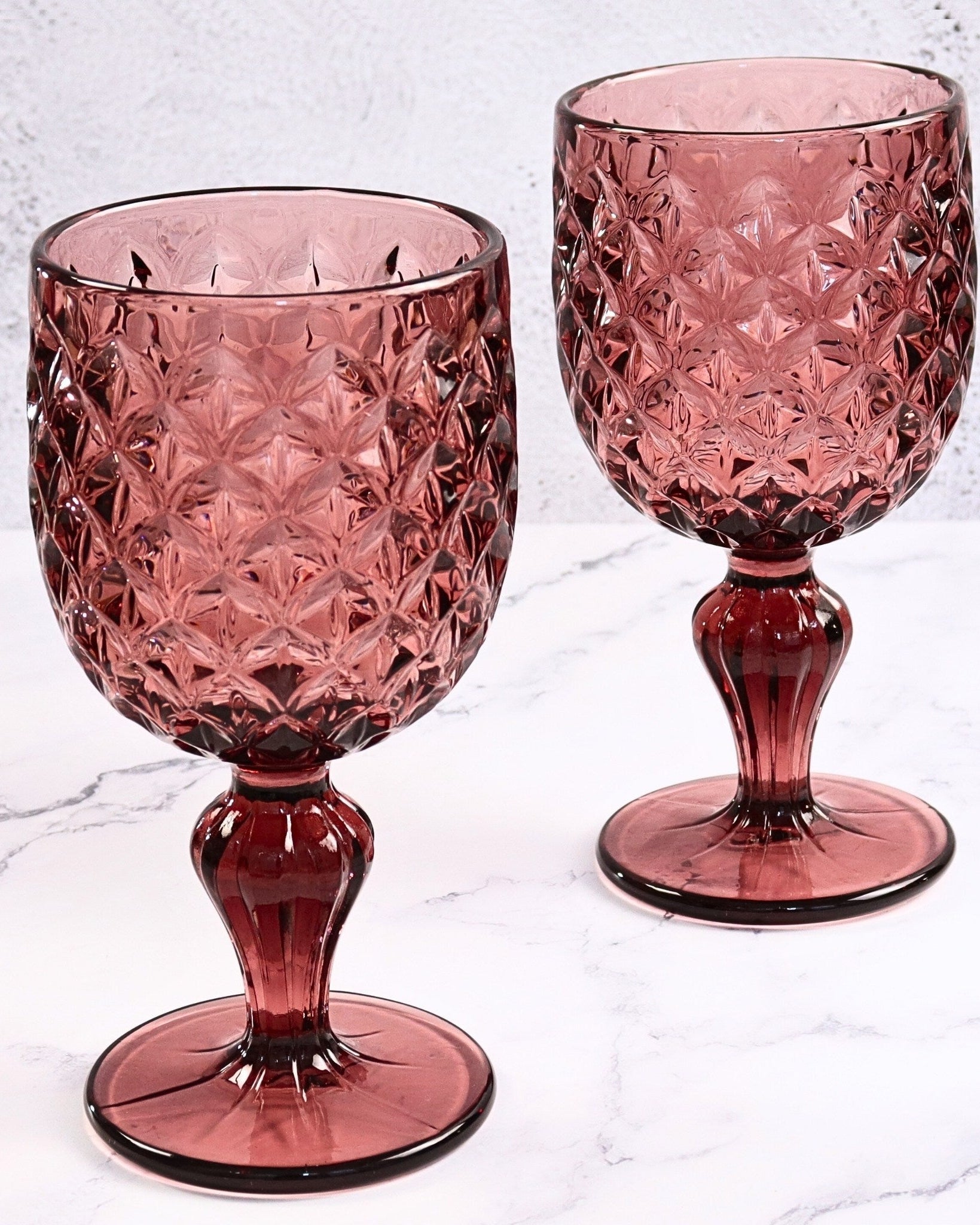 Two purple crystal goblets on a light gray marble surface
