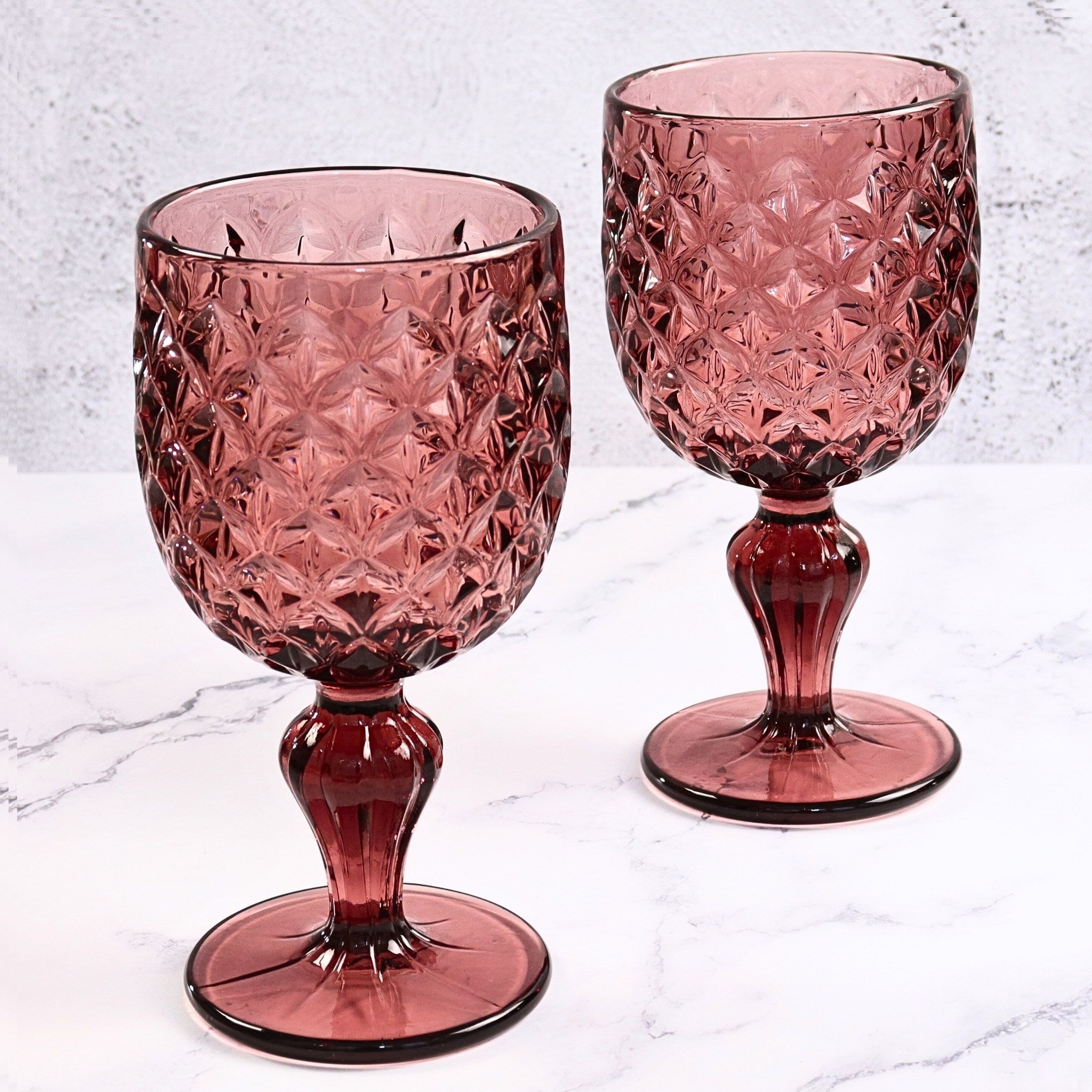 Two purple crystal goblets on a light gray marble surface