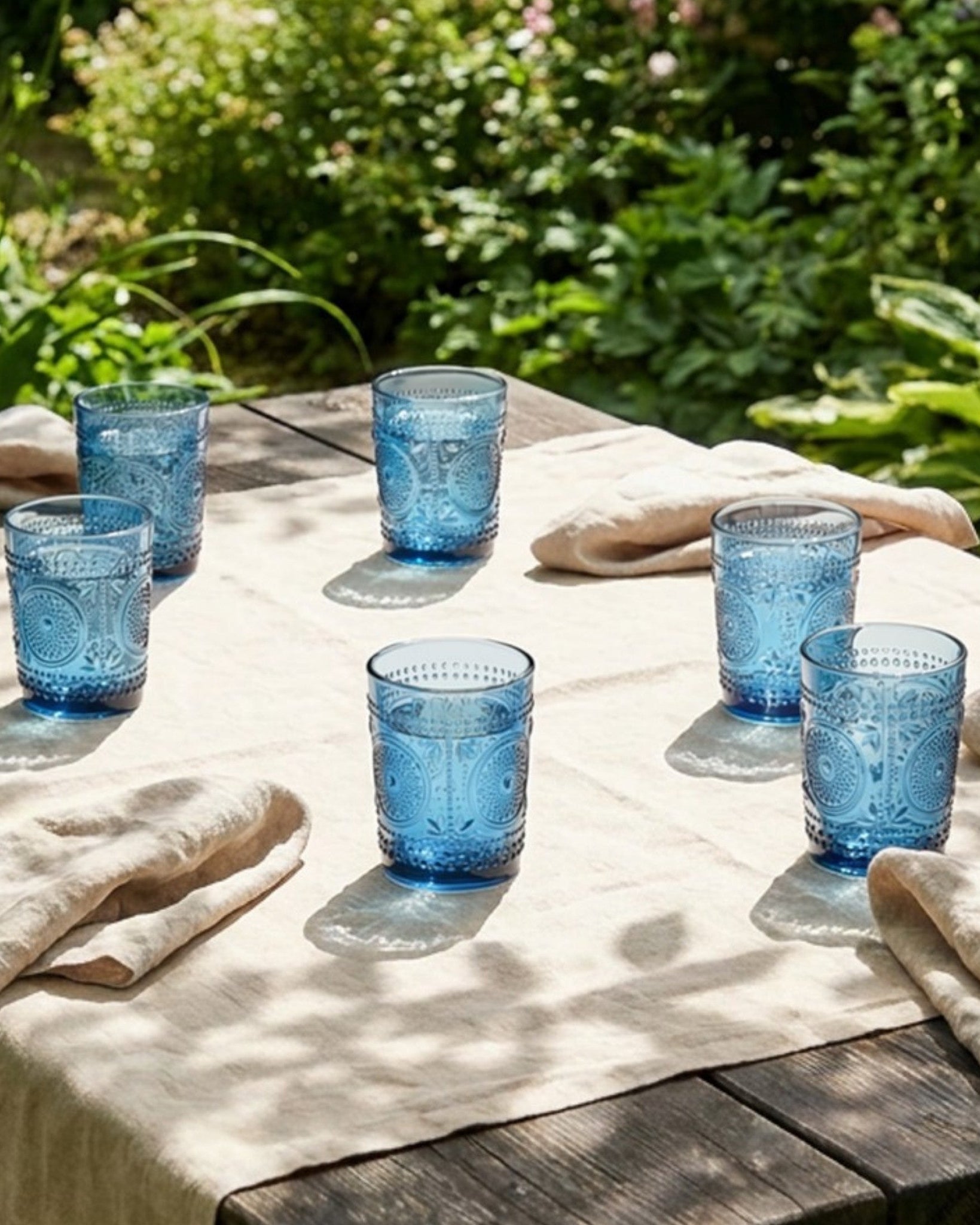 Two blue textured glass tumblers stacked on a white surface with a white curtain background.