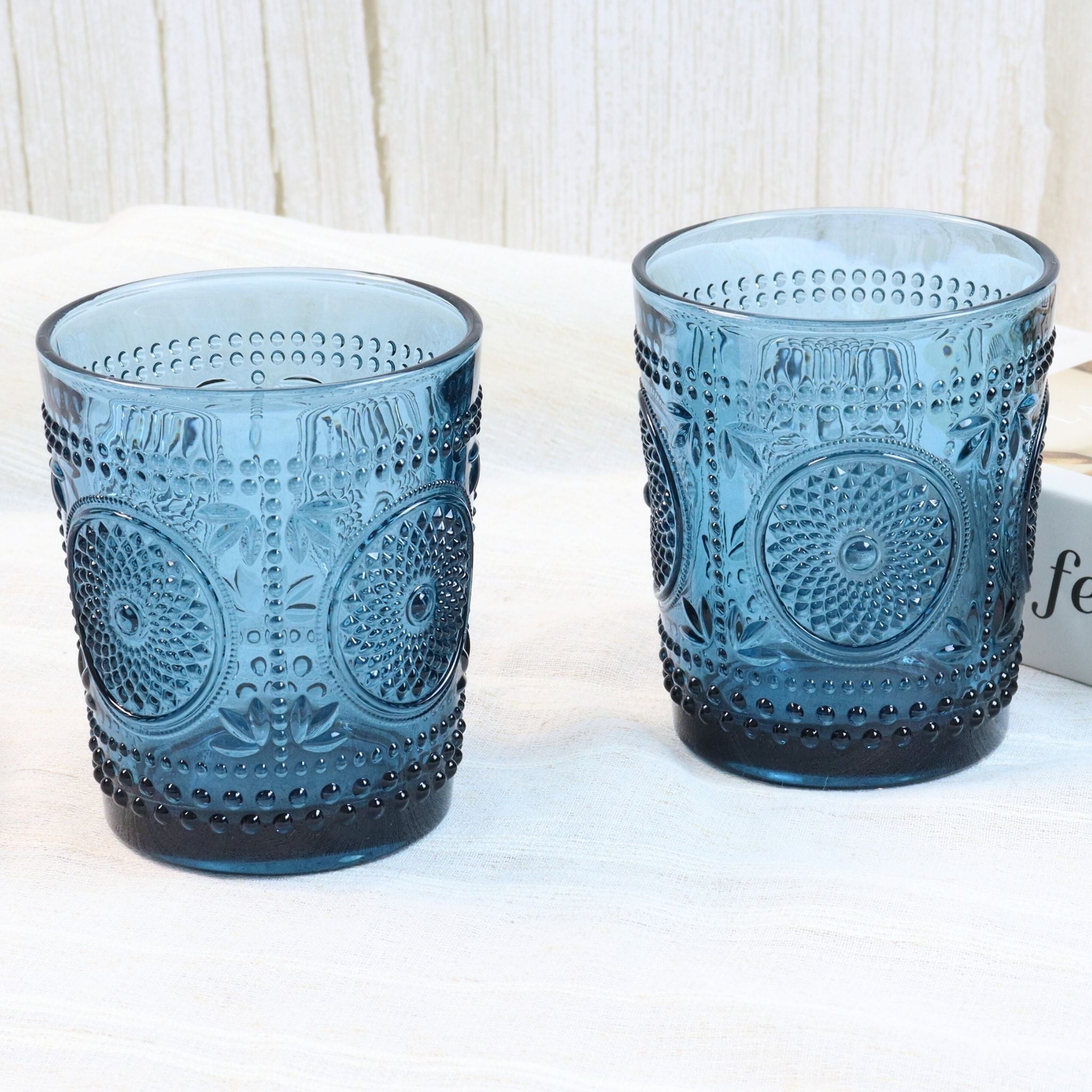 Two blue textured glass tumblers on a white surface with a white textured background.