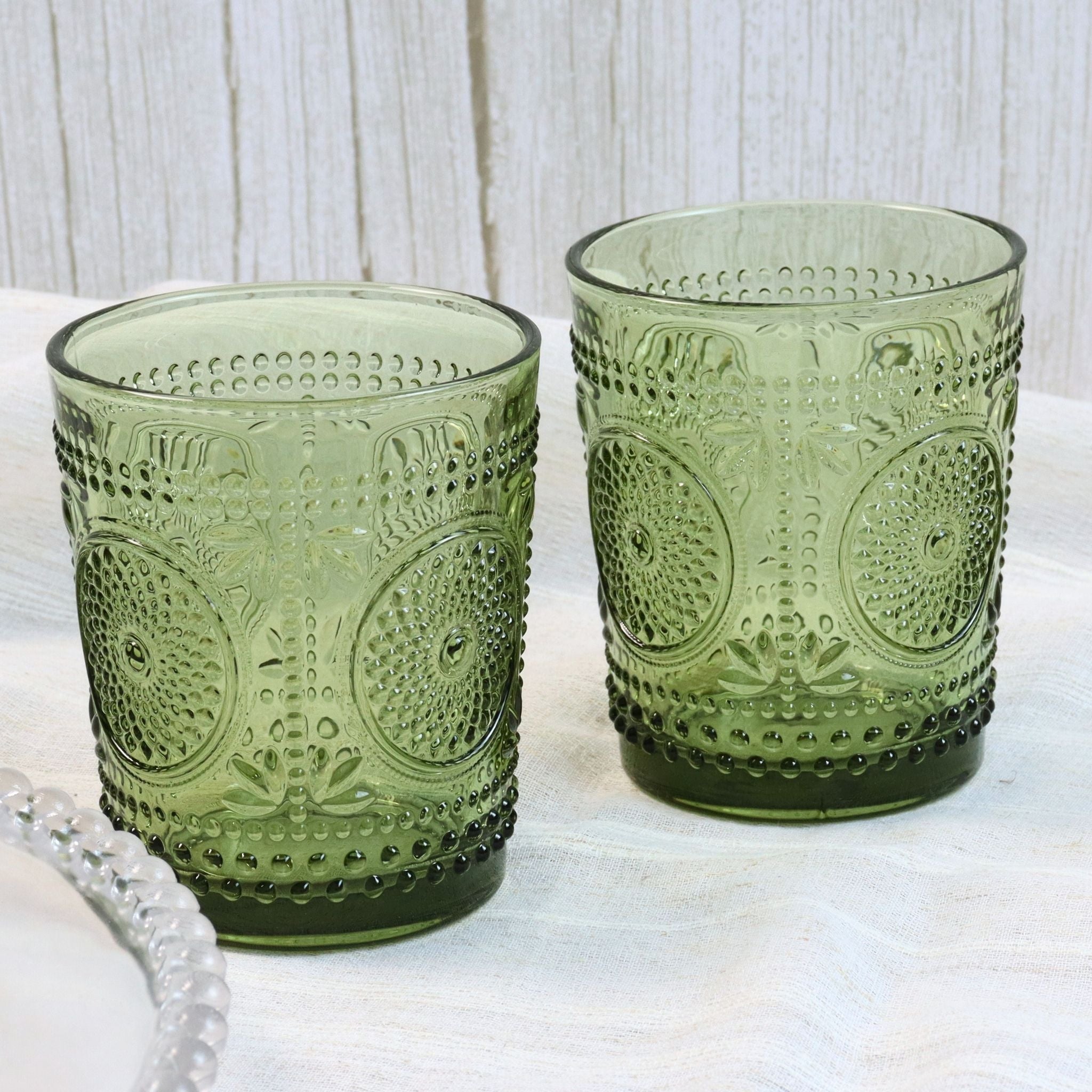 Two green glass tumblers with textured design on a white surface.