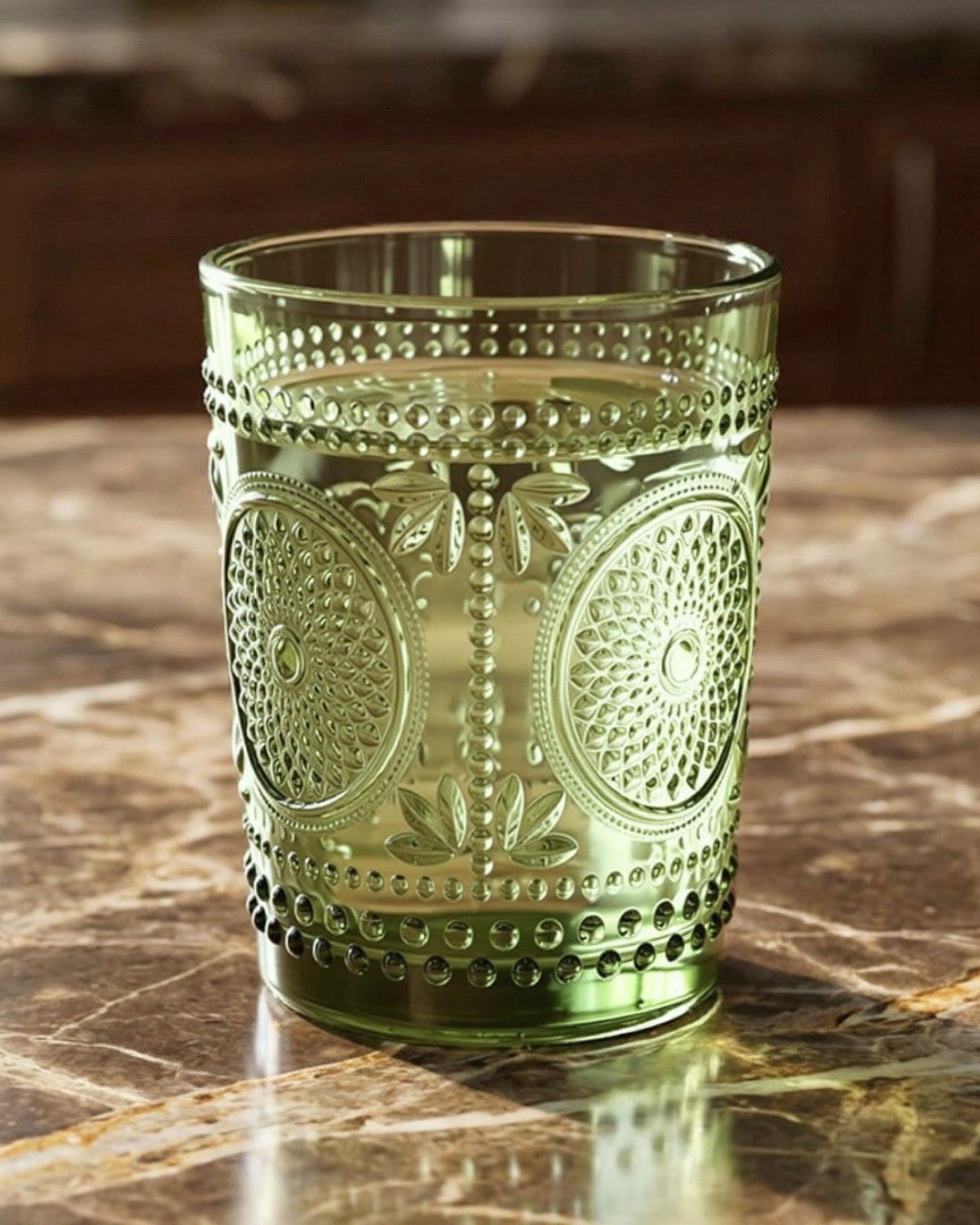 Set of green glass tumblers with embossed designs on a white surface.