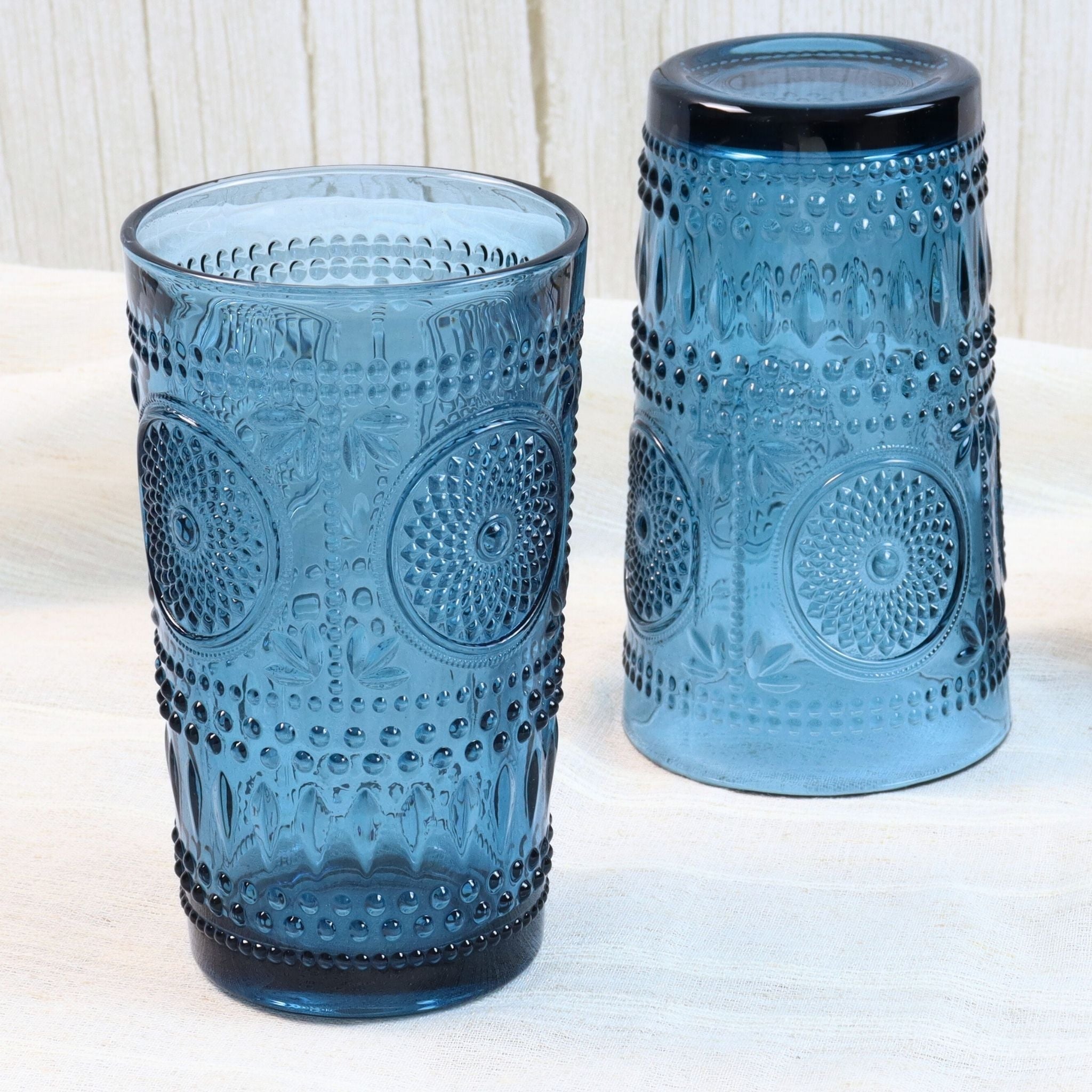 Two blue textured glass tumblers on a white surface with a light wooden background.