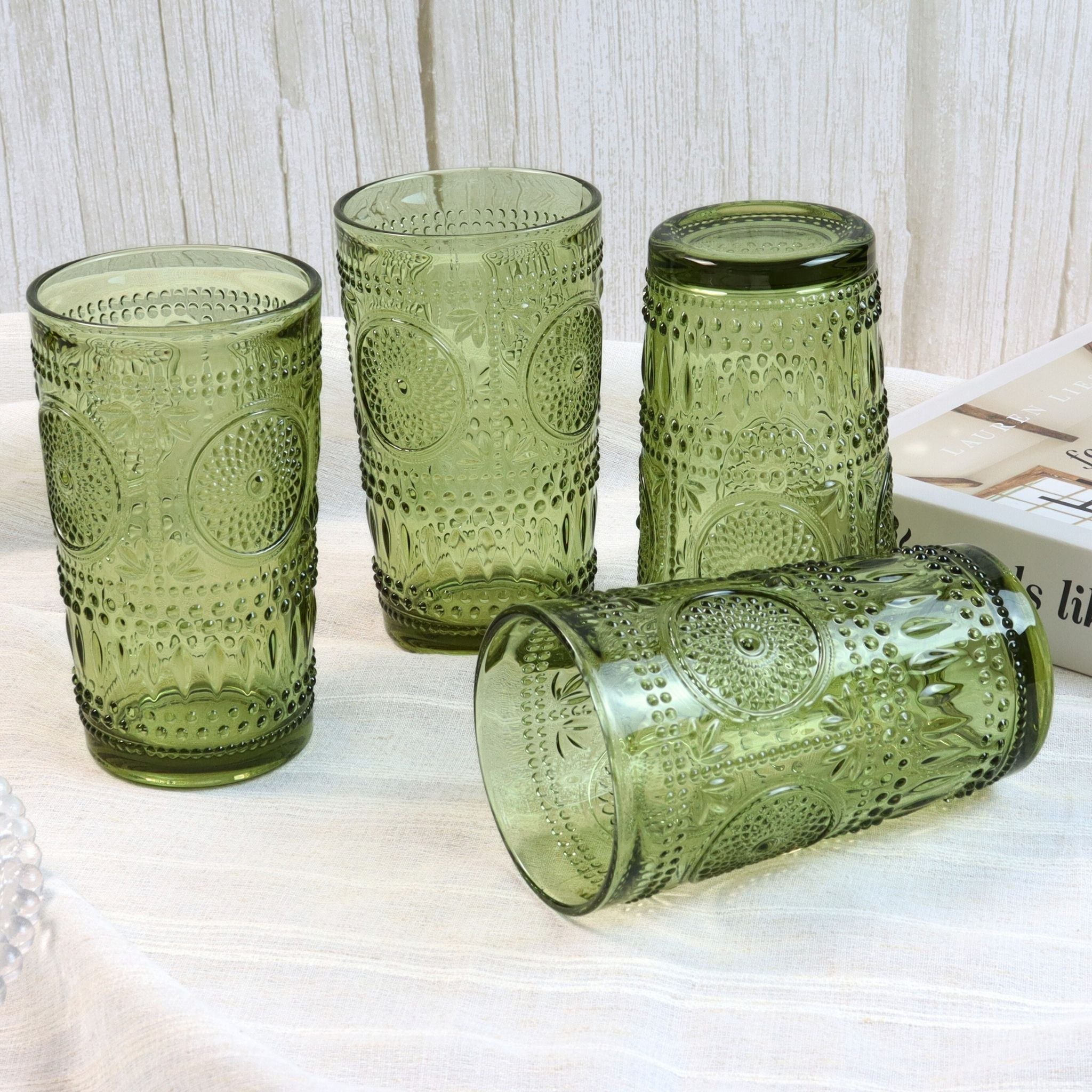 Set of four green patterned glass tumblers on a light surface with a white textured background.