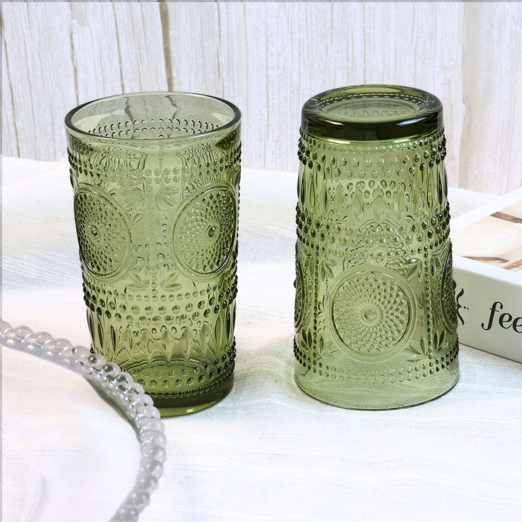 Two green textured glass tumblers on a white surface with a light wooden background.