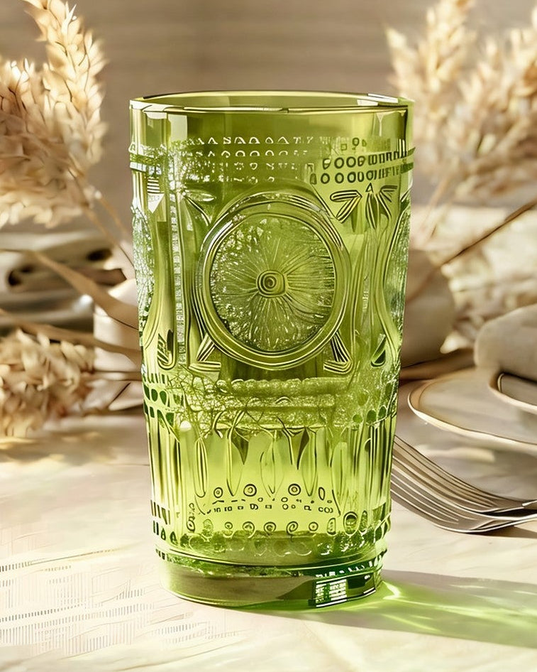 Two green textured glass tumblers on a white surface with a light wooden background.
