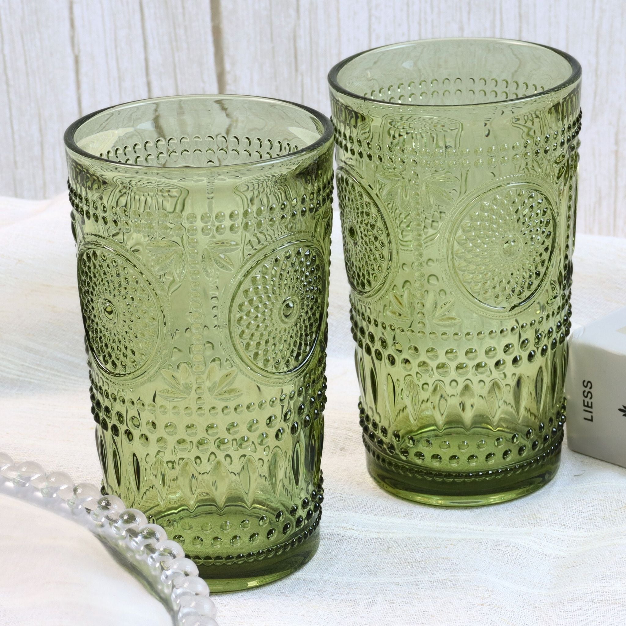 Two green patterned glass tumblers on a white surface with a white box in the background.