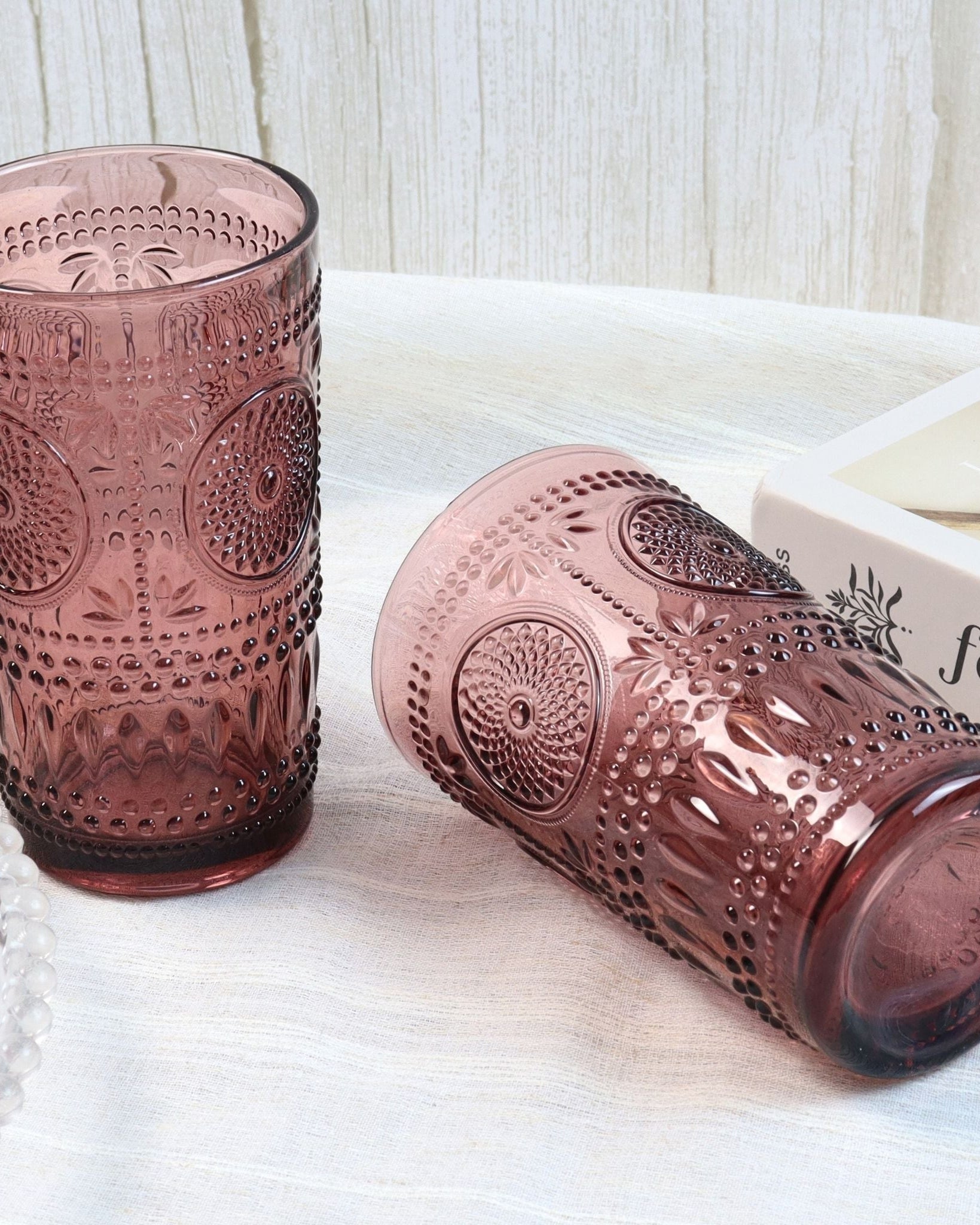 Two pink textured glass tumblers on a white surface with a magazine in the background.