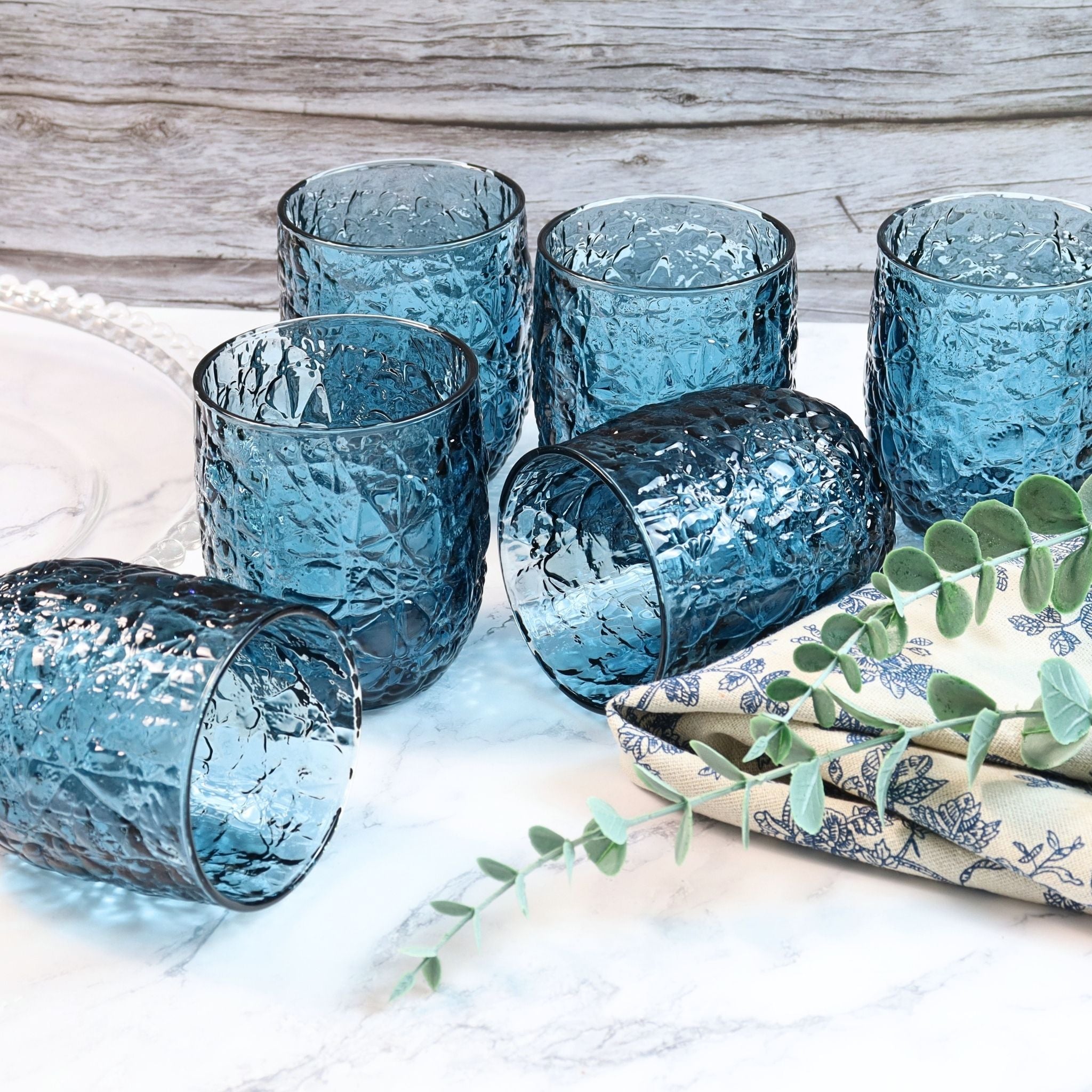 Set of blue textured glasses on a white surface with a wooden background