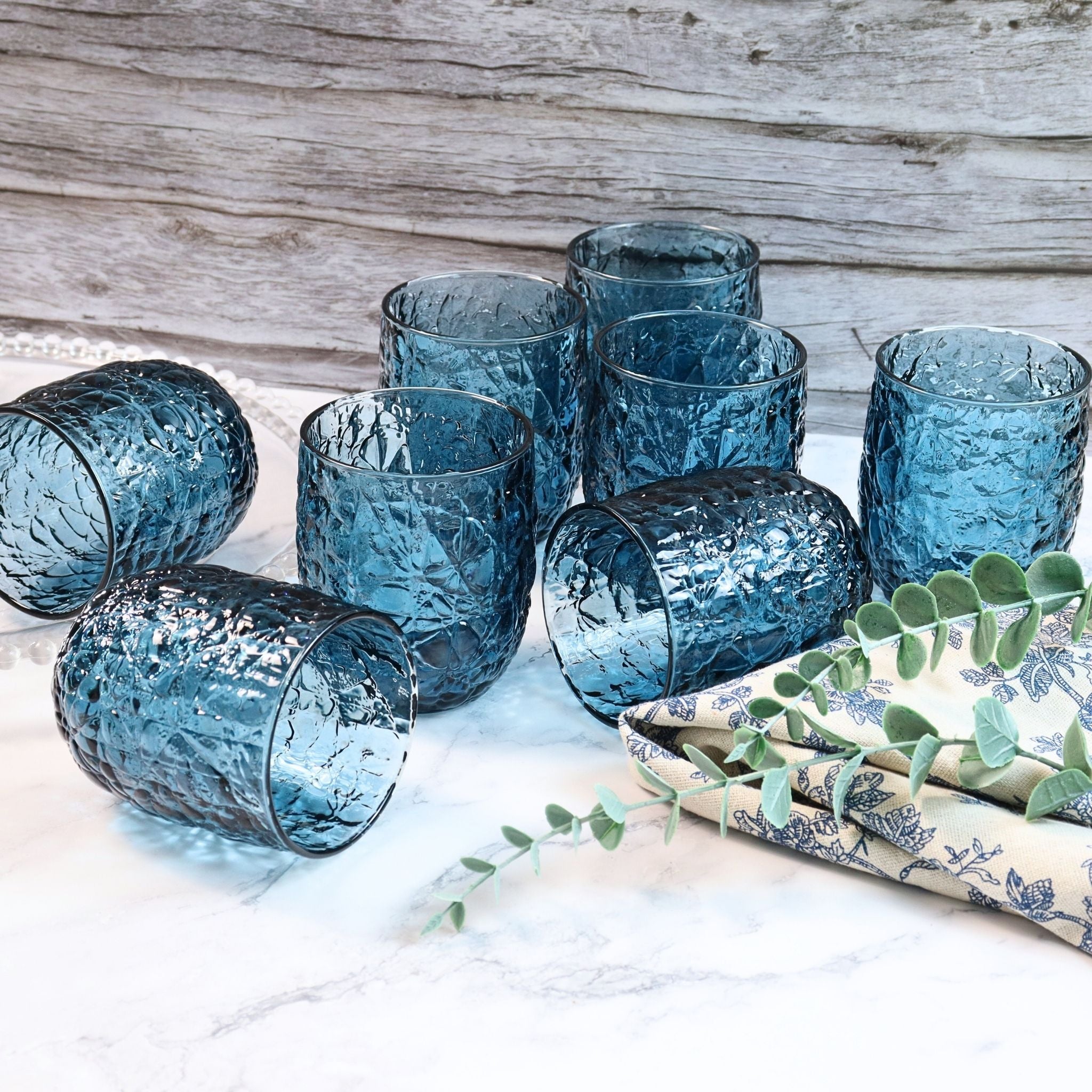 Set of blue glass tumblers on a white surface with a wooden background
