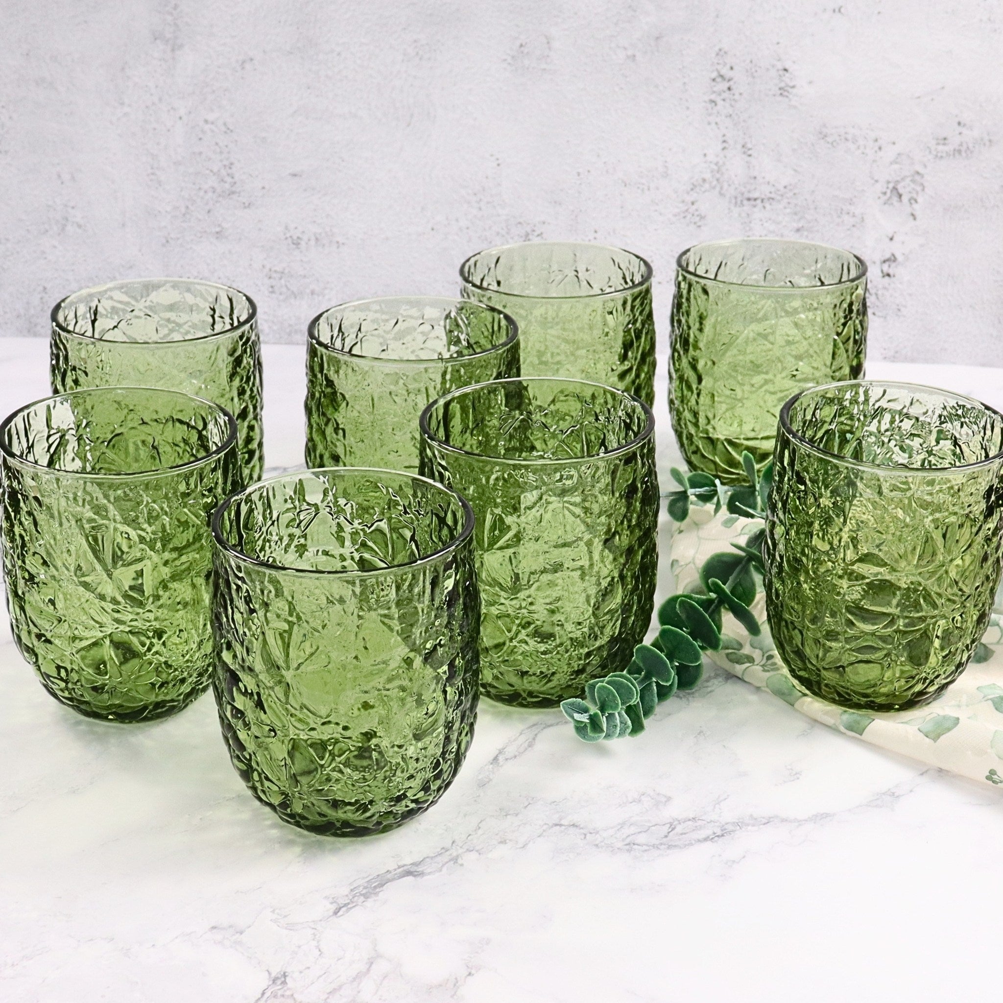 Set of green textured glass tumblers on a marble surface with a light gray background