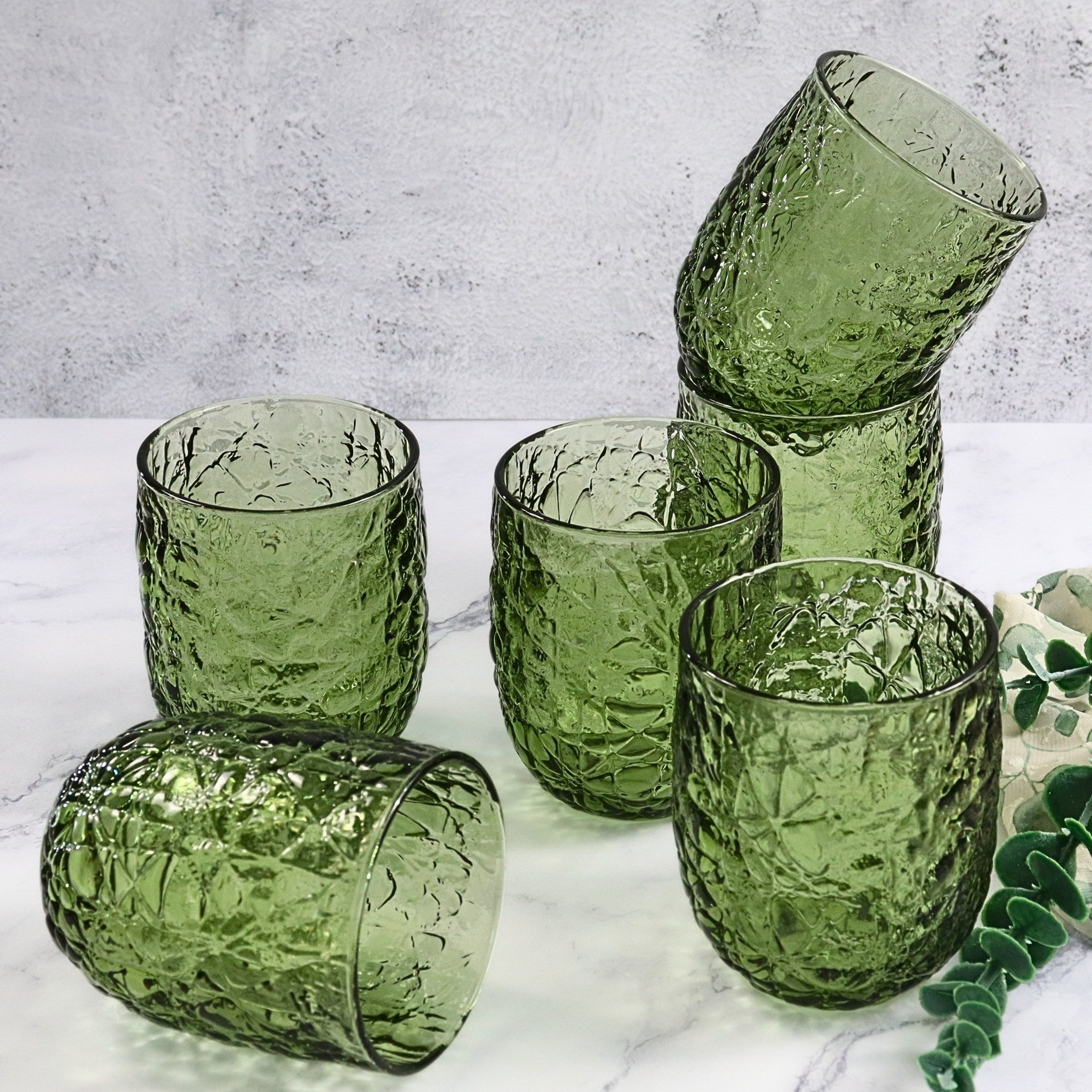 Set of green textured glass tumblers on a marble surface with a light gray background