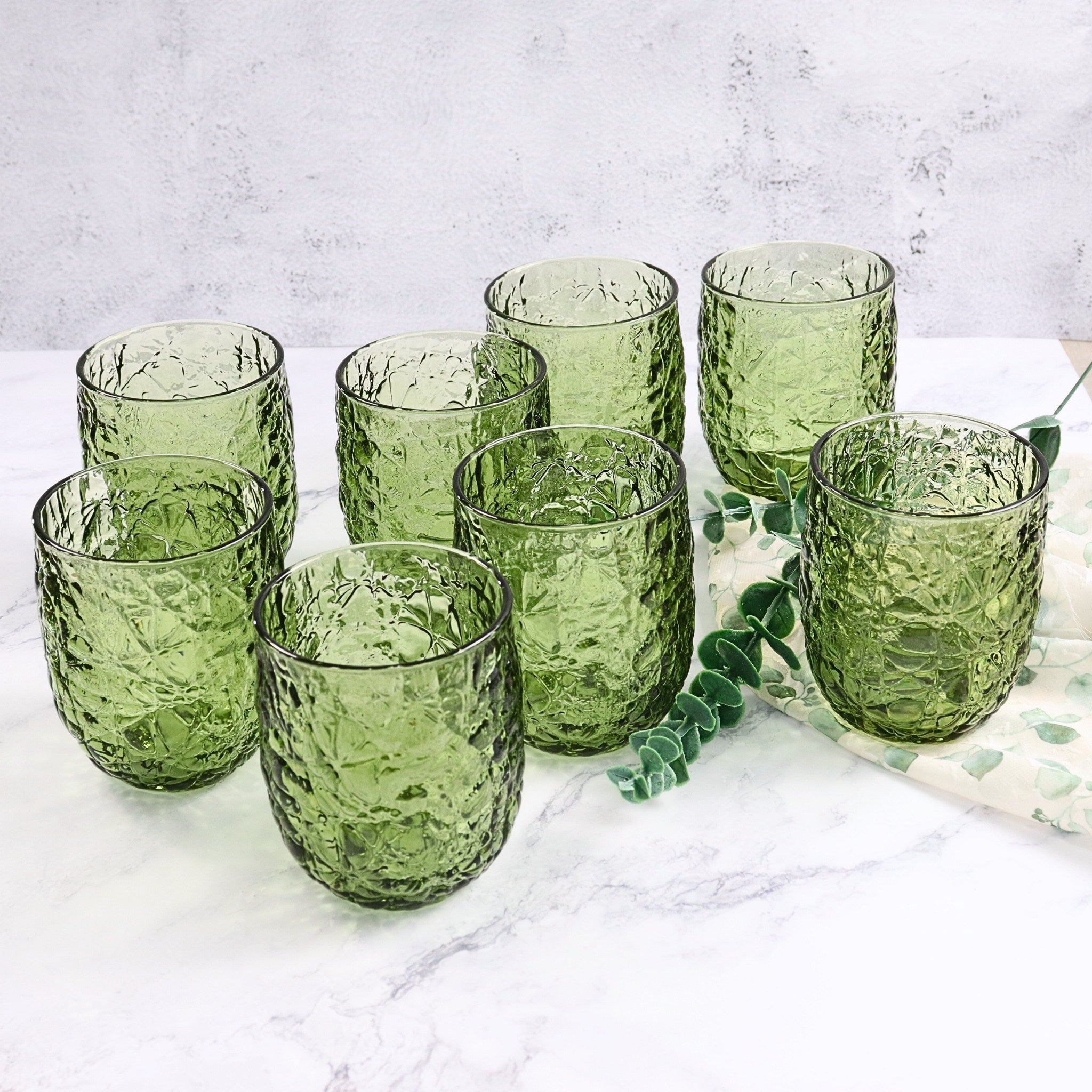 Set of green glass tumblers on a marble surface with a white background