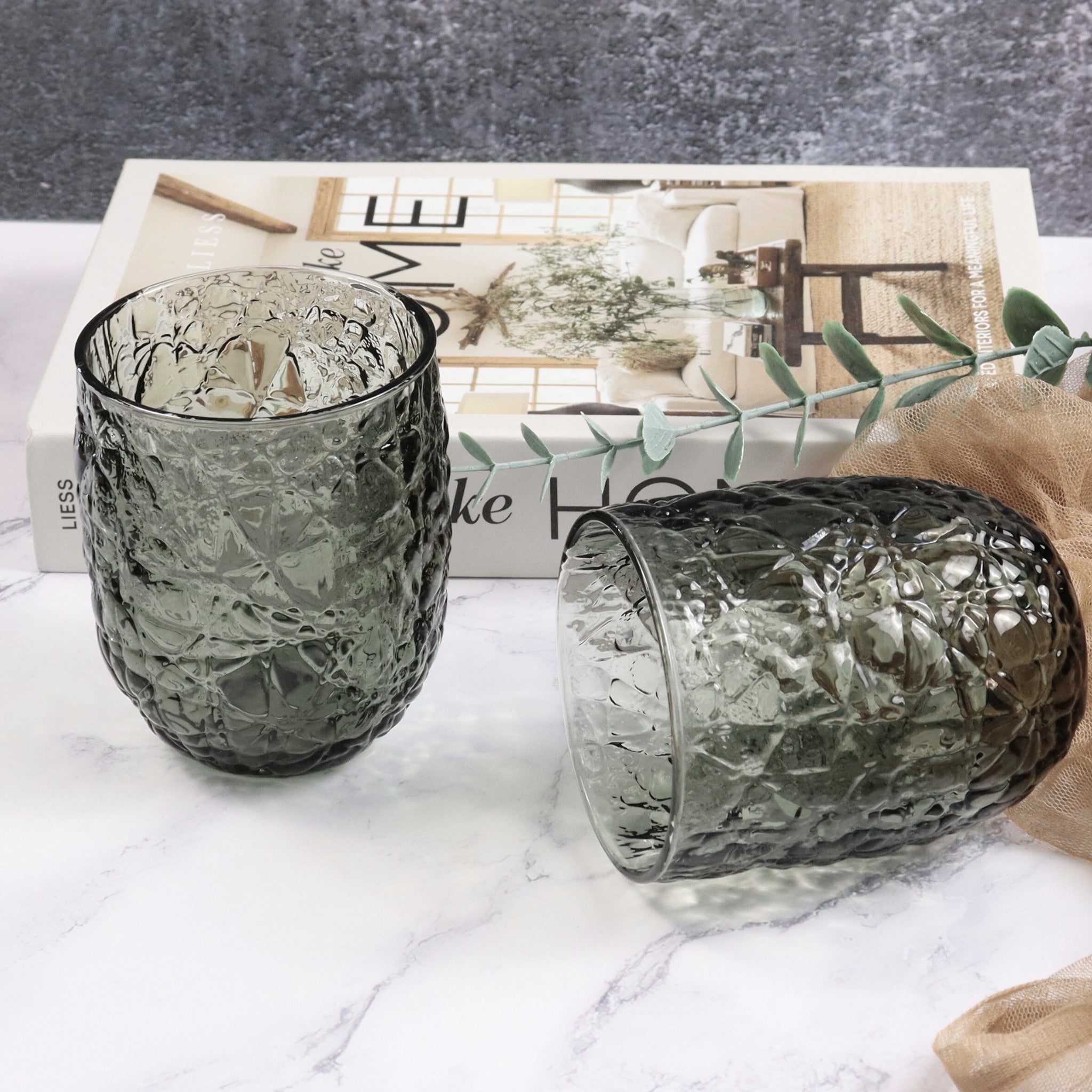 Two textured glass tumblers on a marble surface with a magazine in the background.