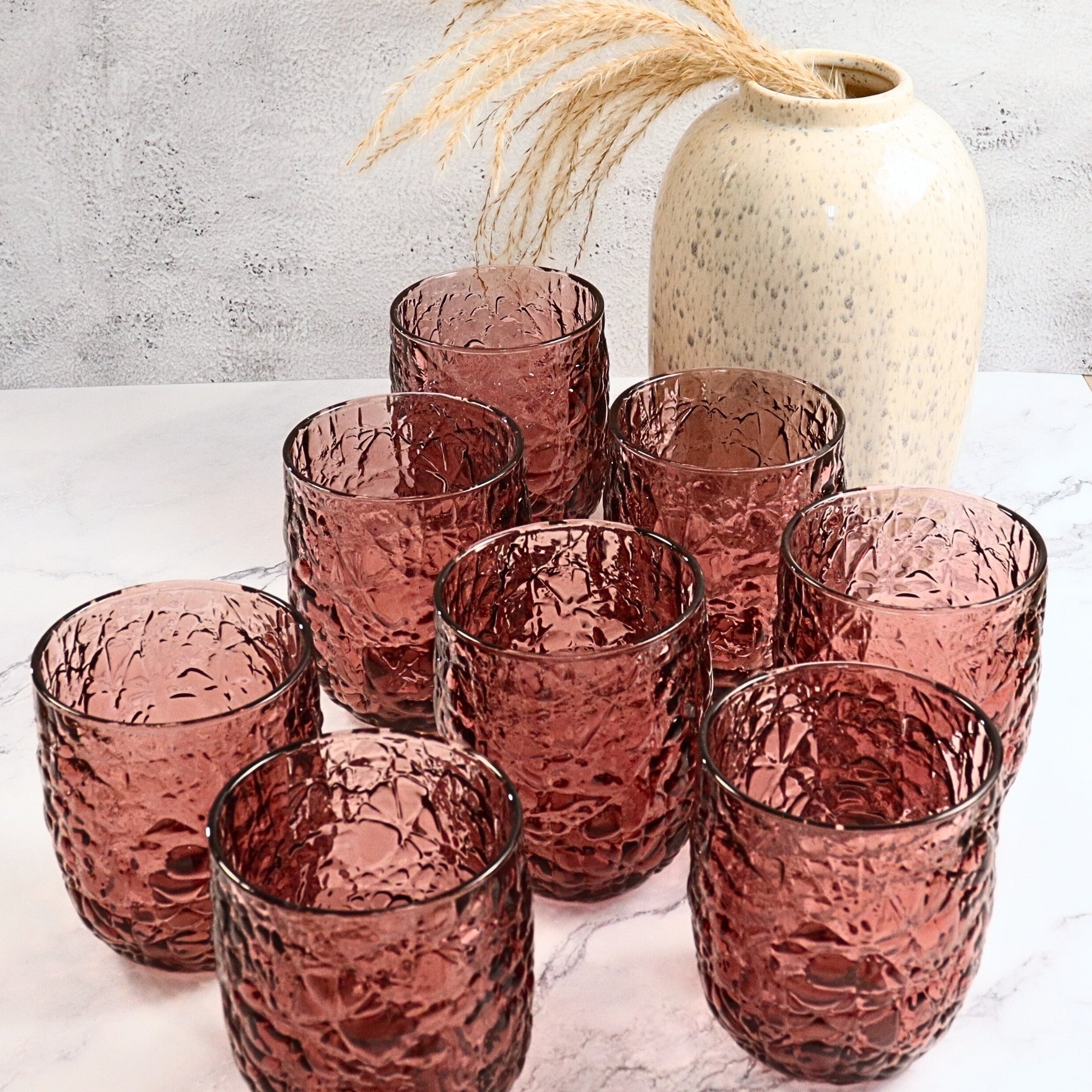 Set of purple textured glass tumblers on a light surface with a neutral vase in the background.