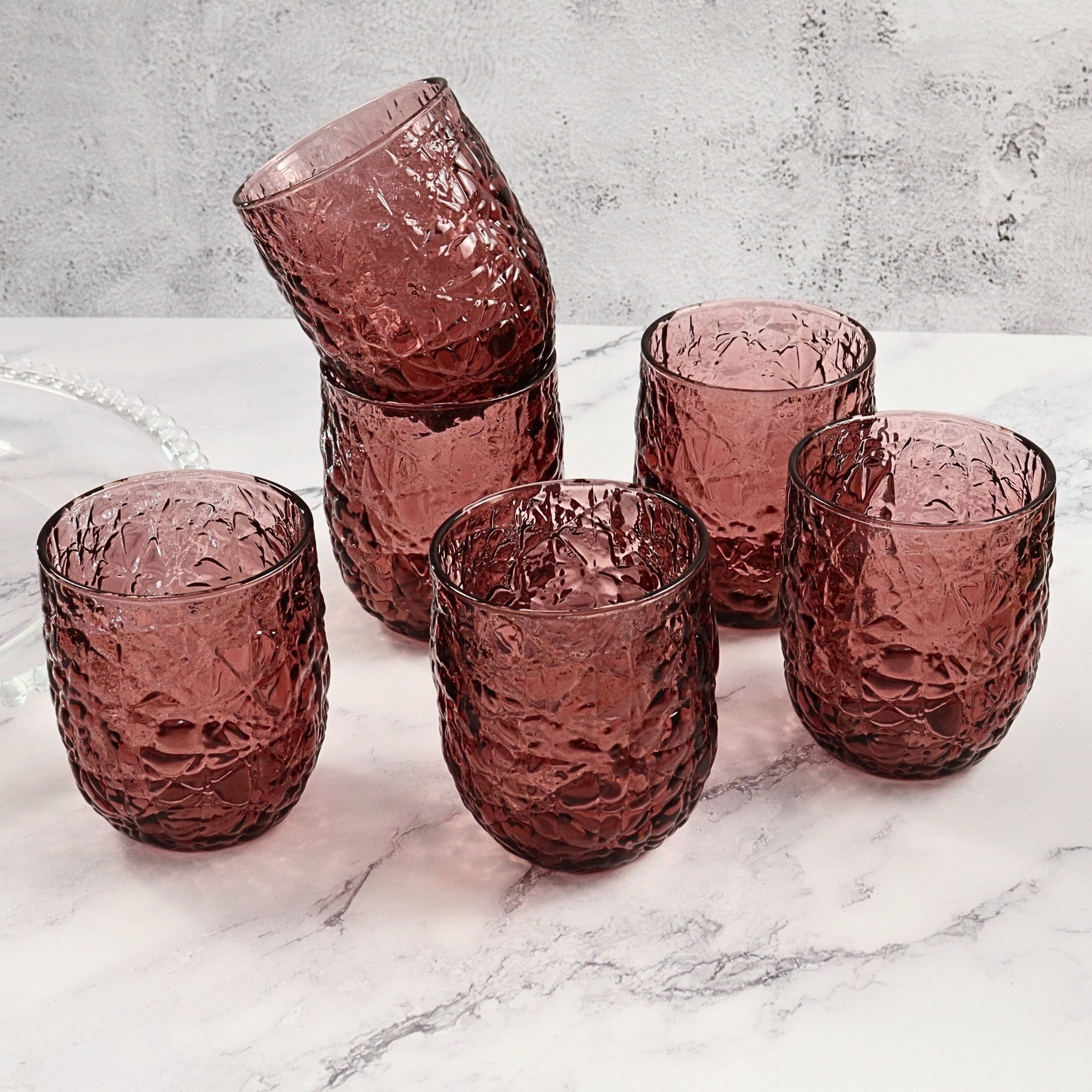 Set of purple textured glass tumblers on a marble surface with a gray concrete wall background.