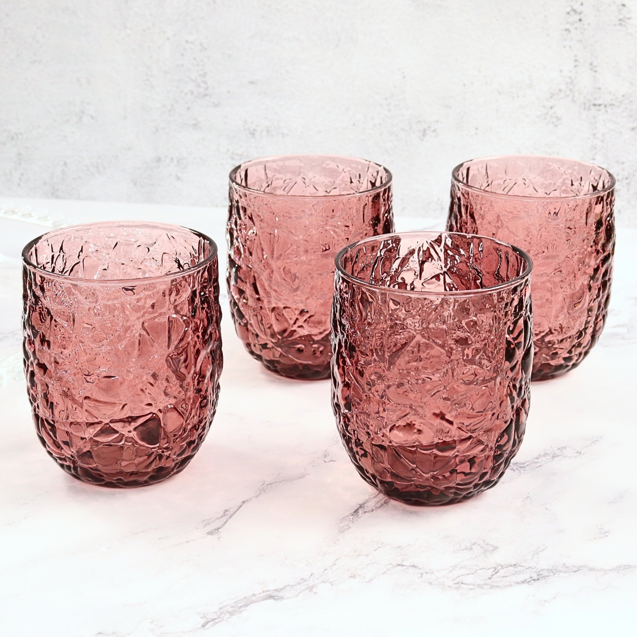 Four purple textured glass tumblers on a light marble surface