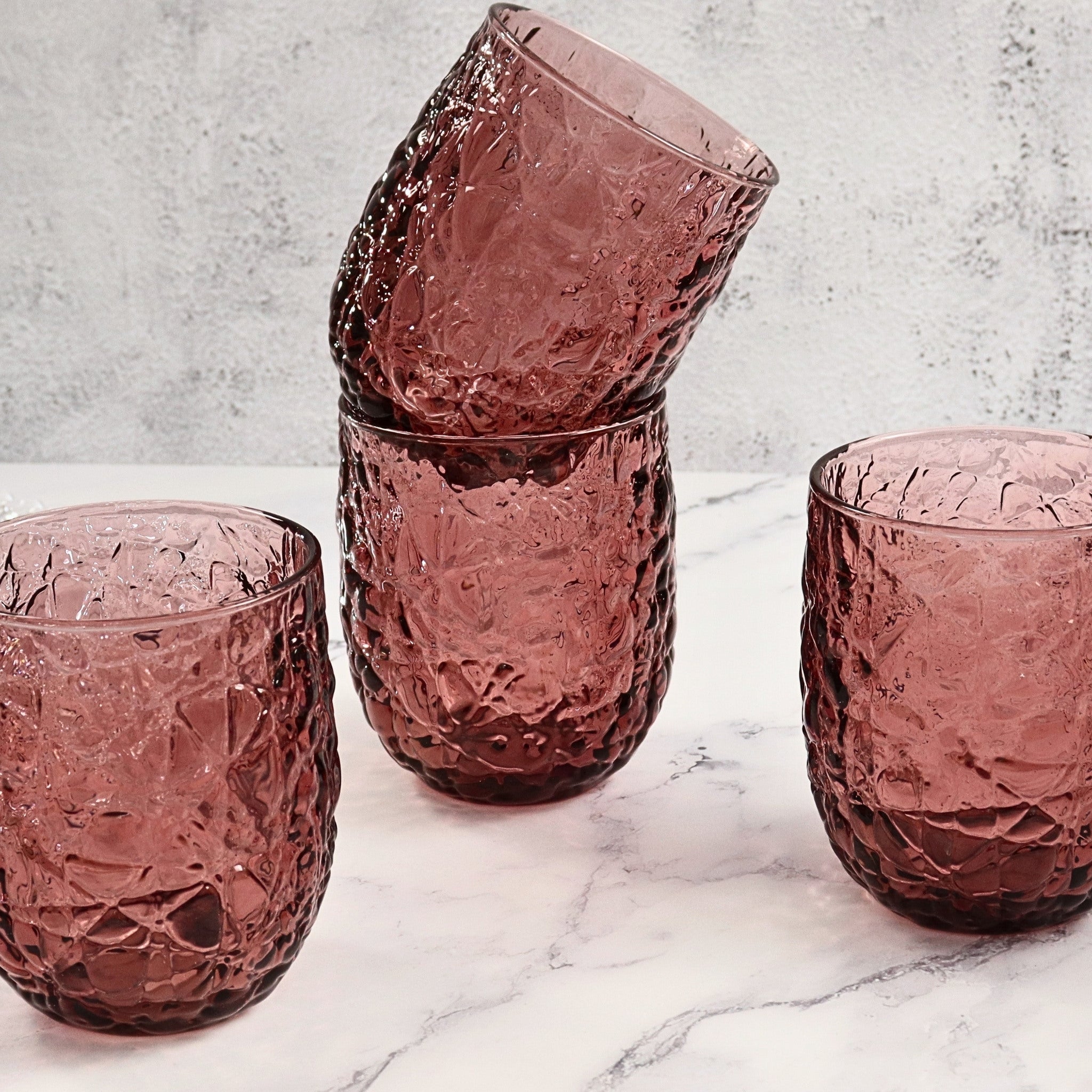 Set of purple textured glass tumblers on a marble surface with a light gray background