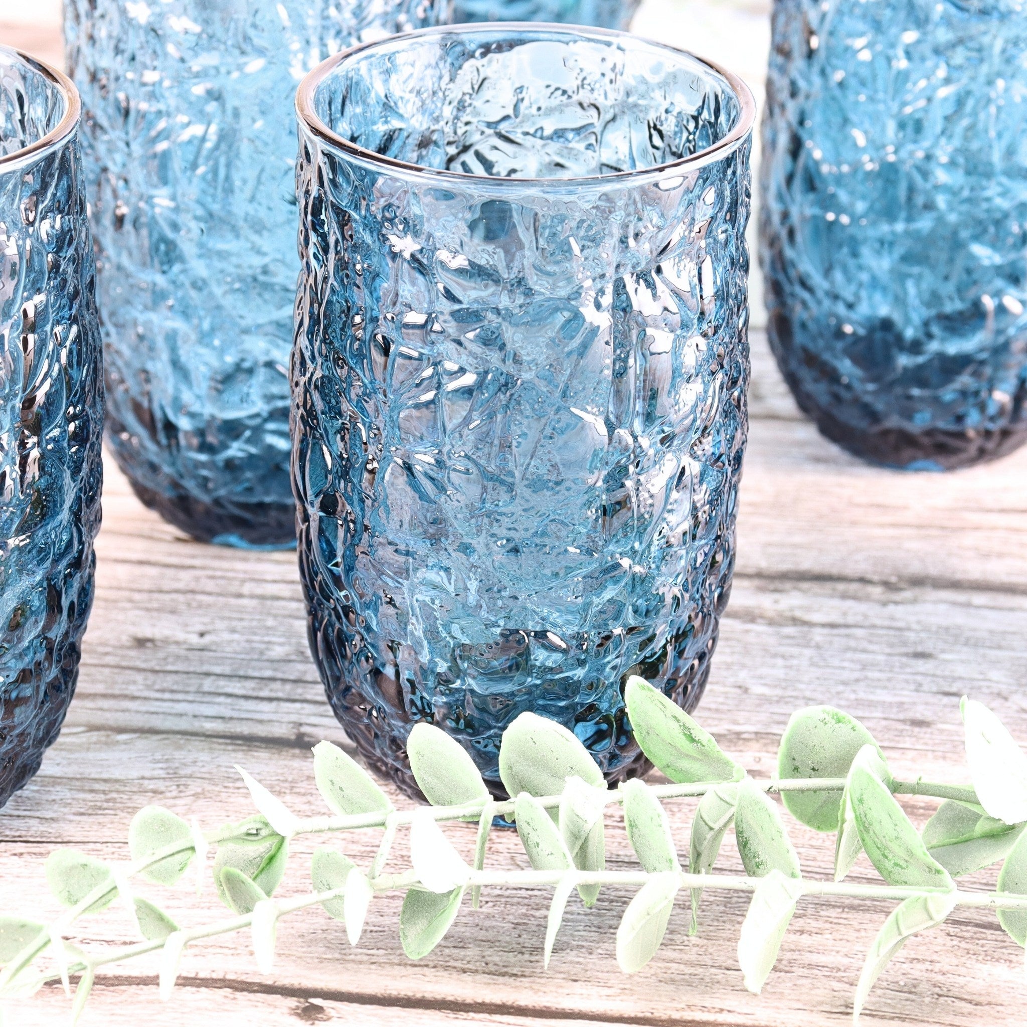 Blue textured glass tumblers on a wooden surface with green leaves.