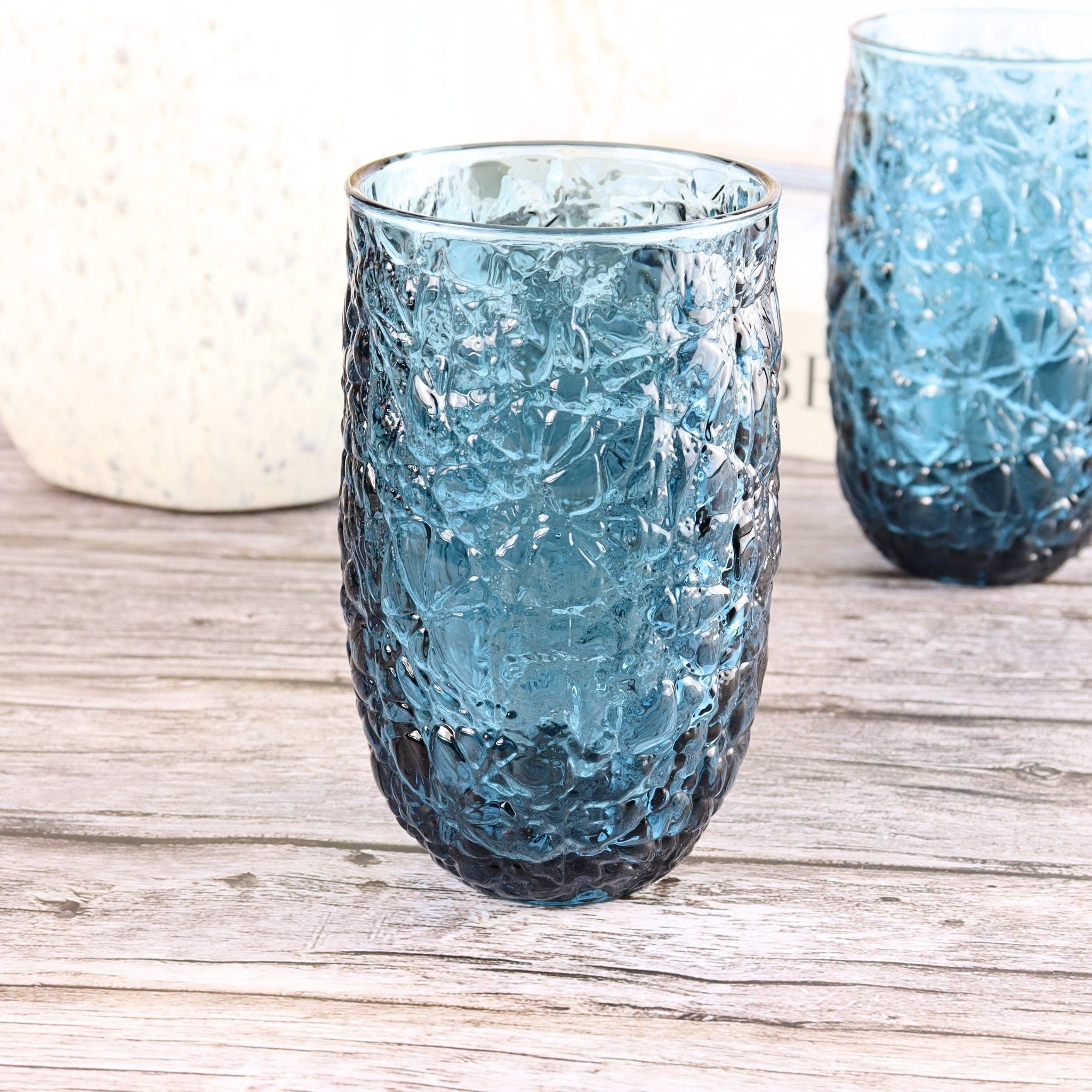 Two textured blue glass tumblers on a wooden surface
