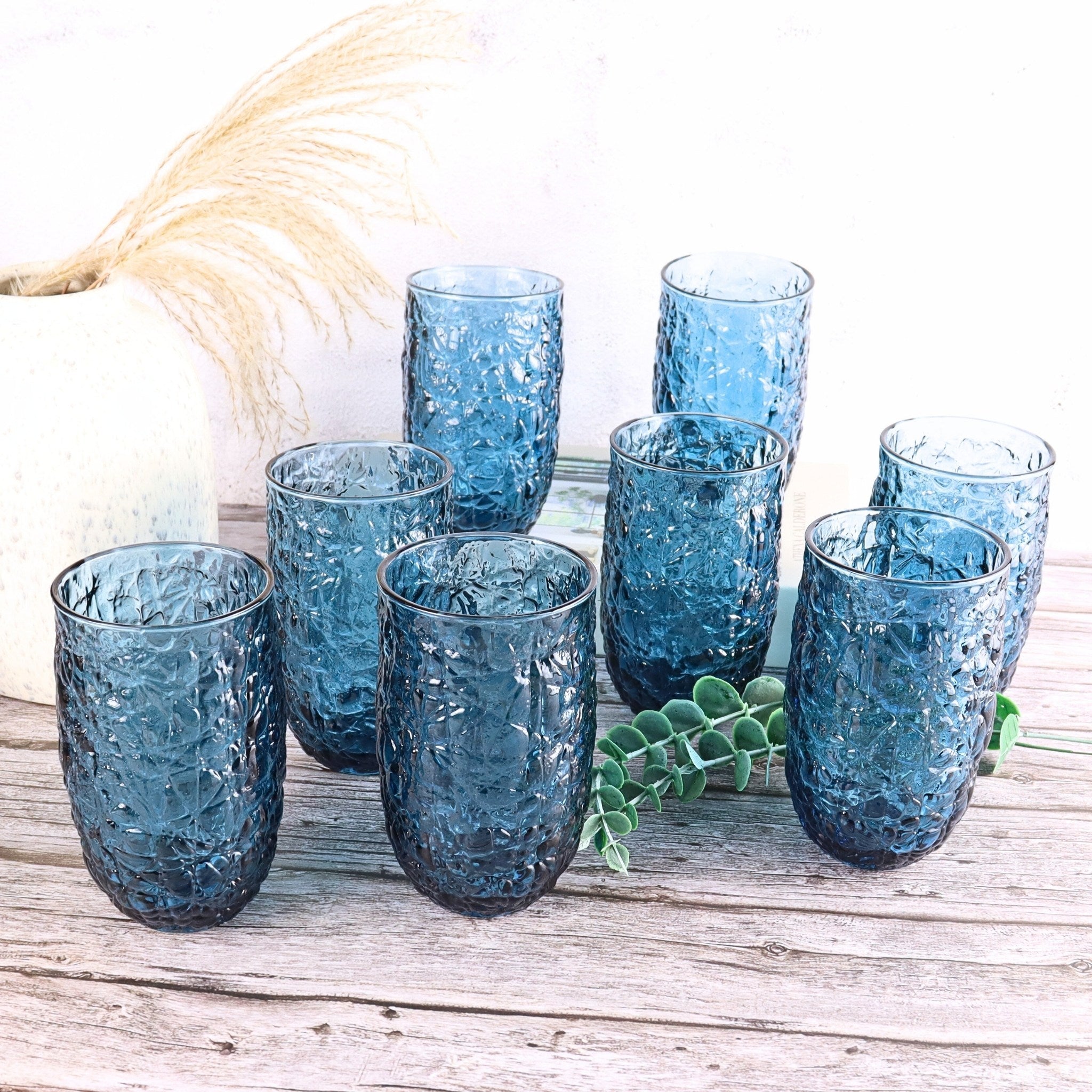 Set of 8 blue textured glasses on a wooden surface with a white background