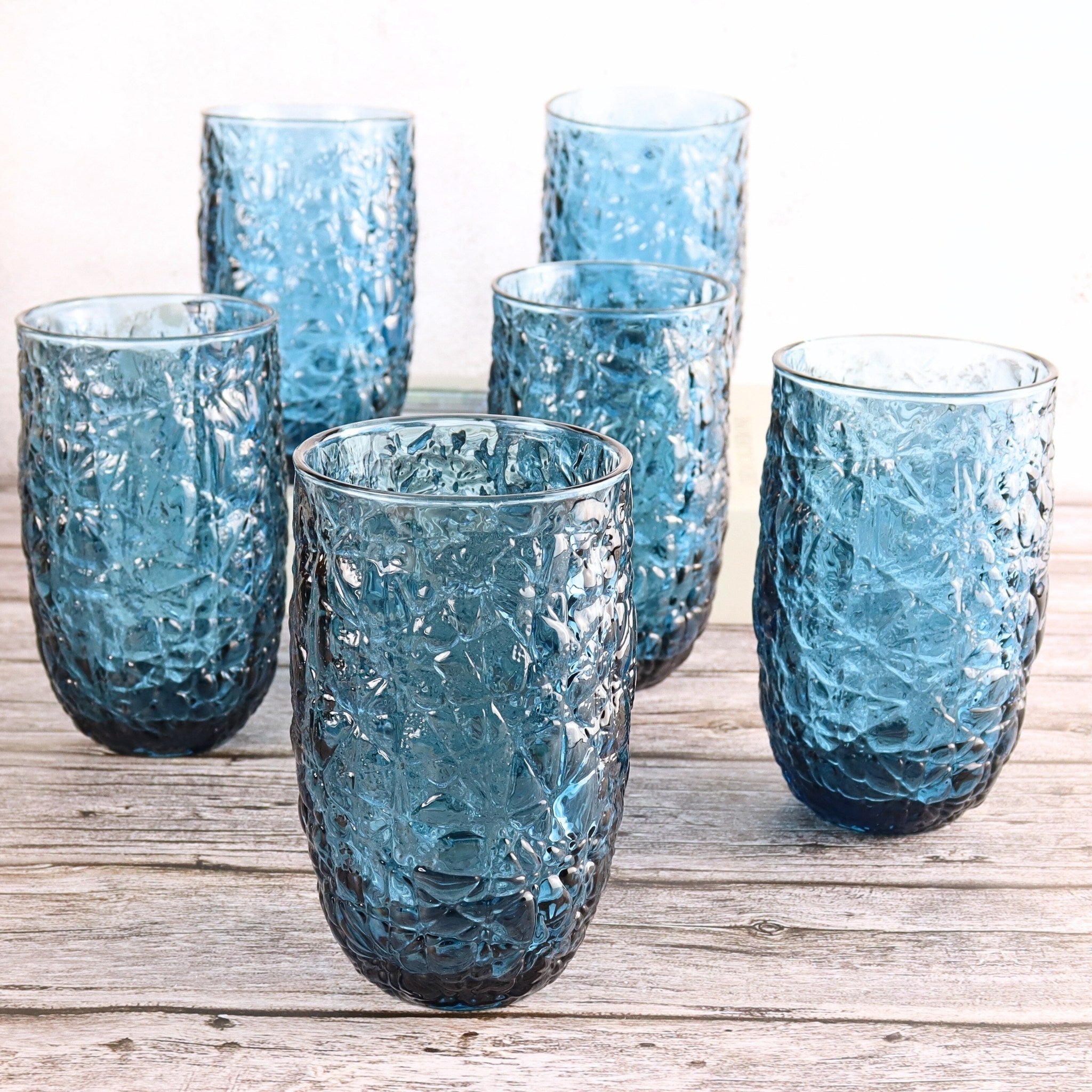 Set of six textured blue glasses on a wooden surface