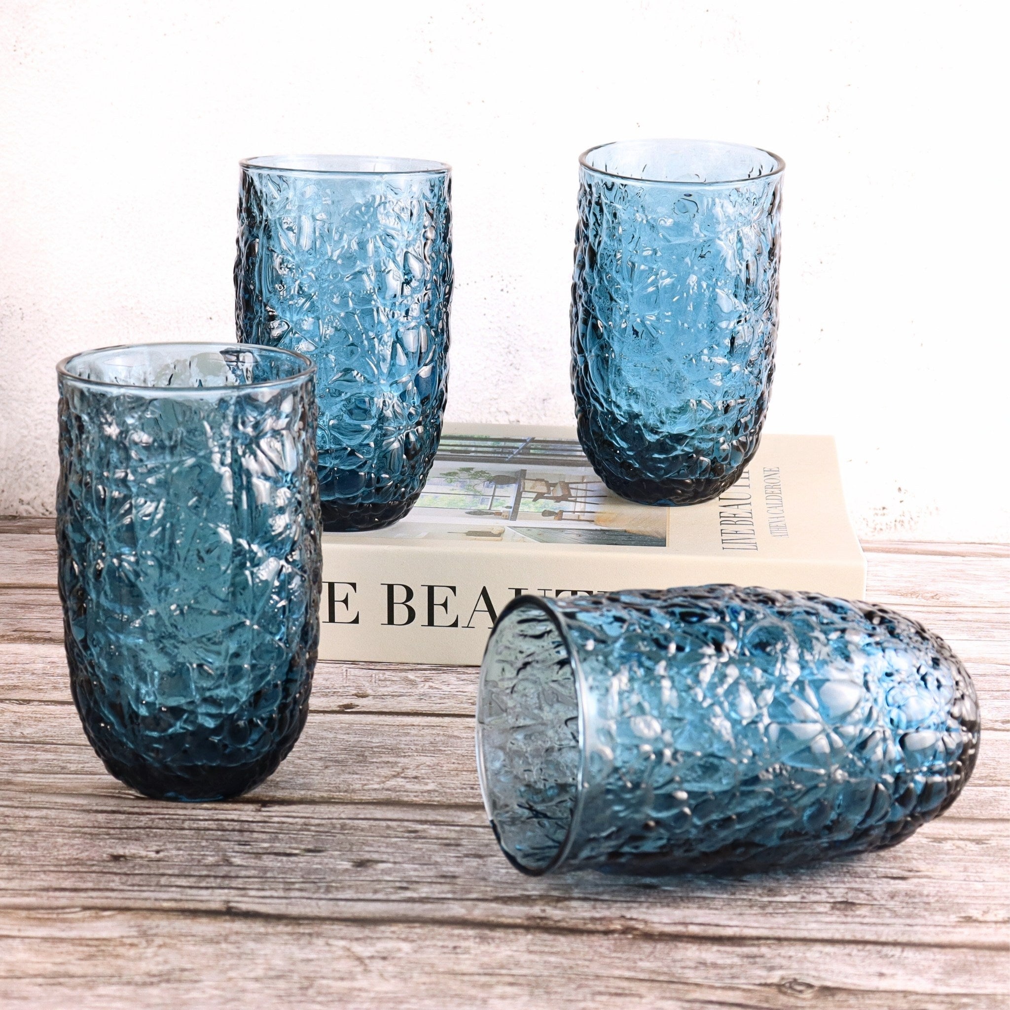 Set of four blue textured glass tumblers on a wooden surface with a newspaper underneath.