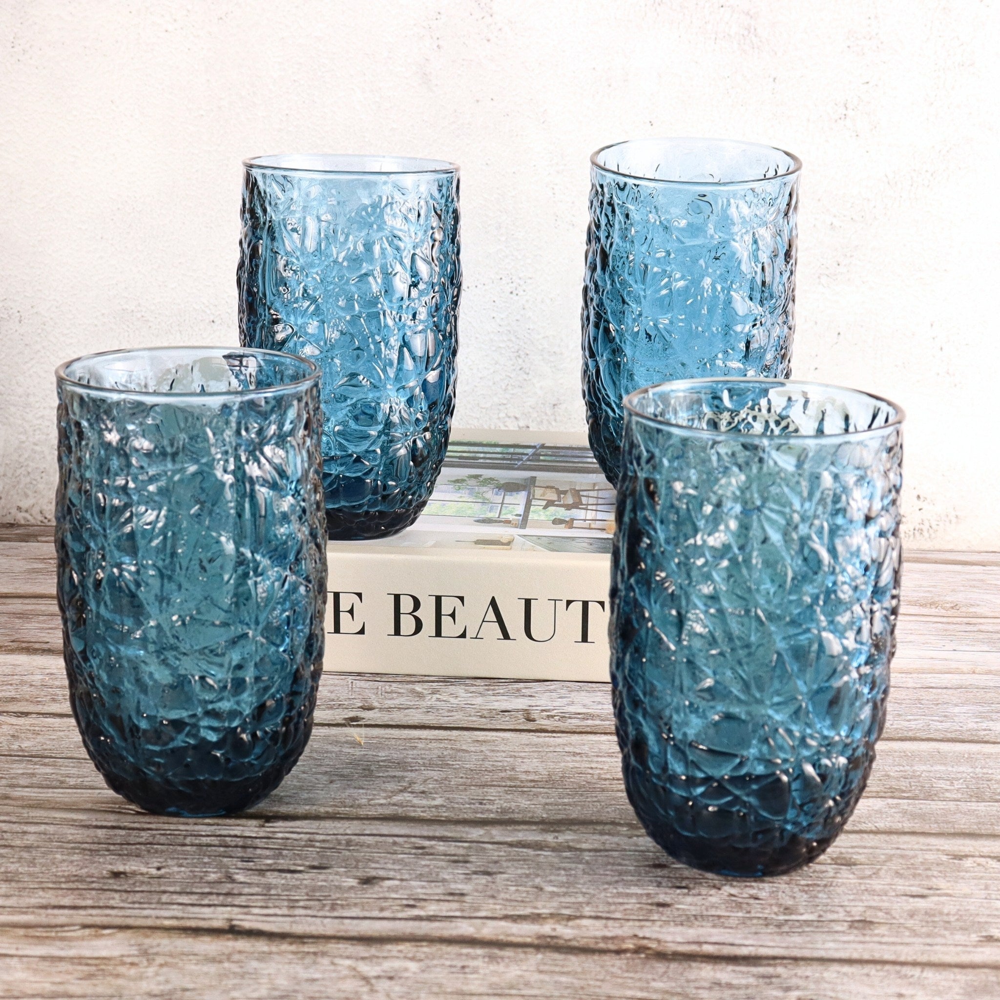 Four textured blue glasses on a wooden surface with a blurred background