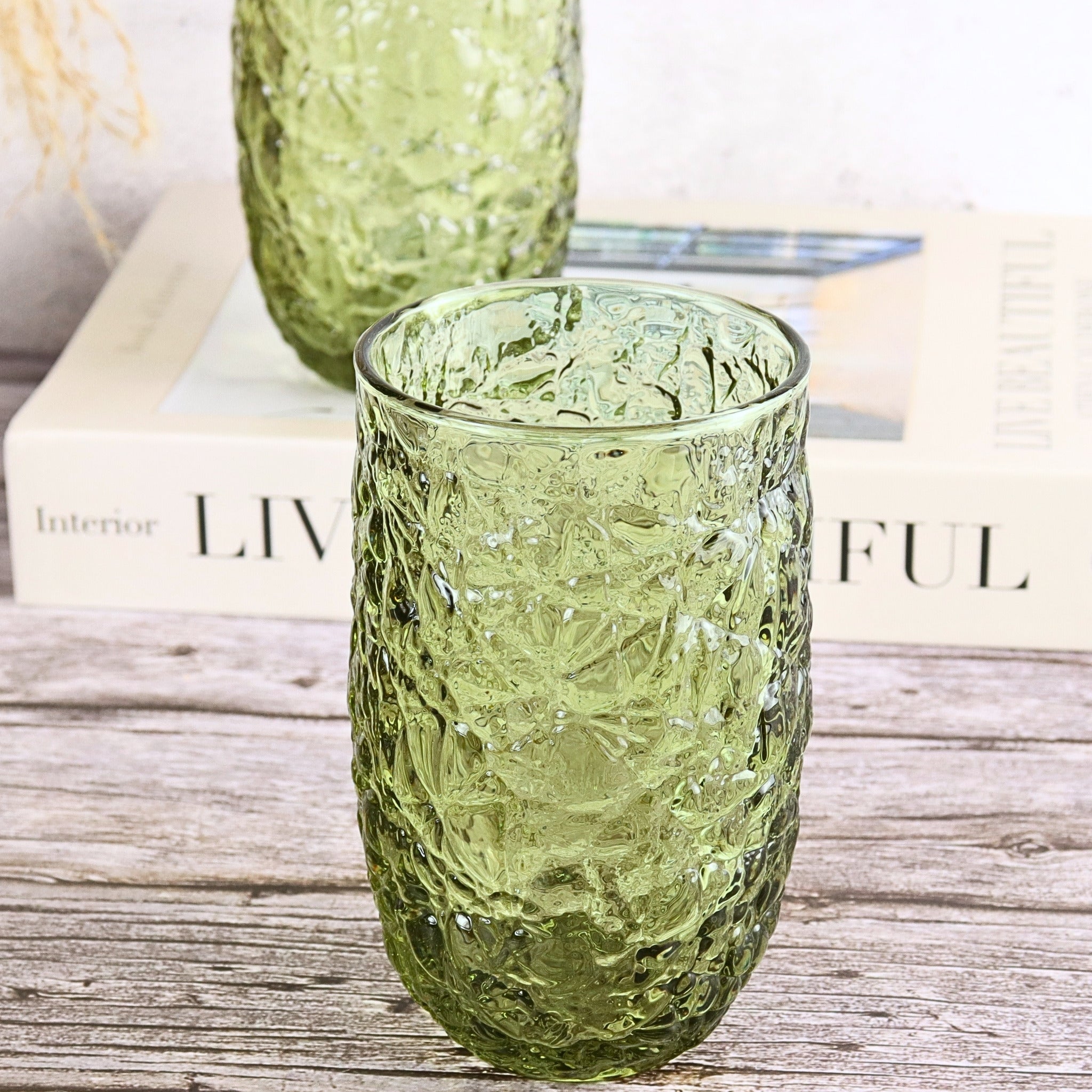 Green textured glass tumblers on a wooden surface with books in the background