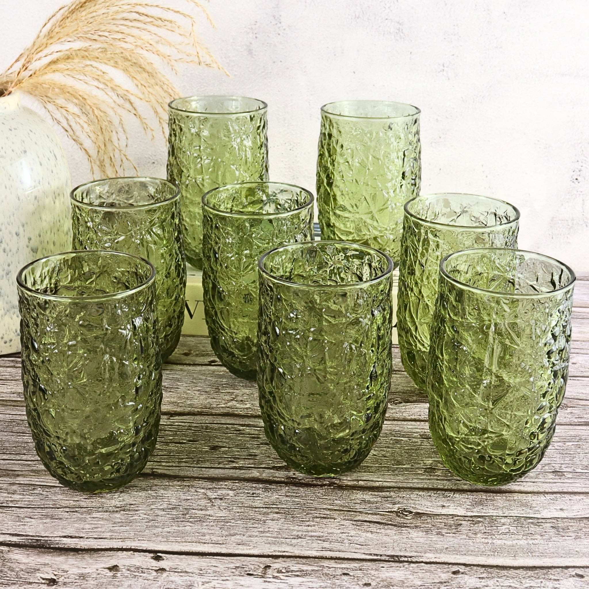 Set of green textured glass tumblers on a wooden surface with a white background