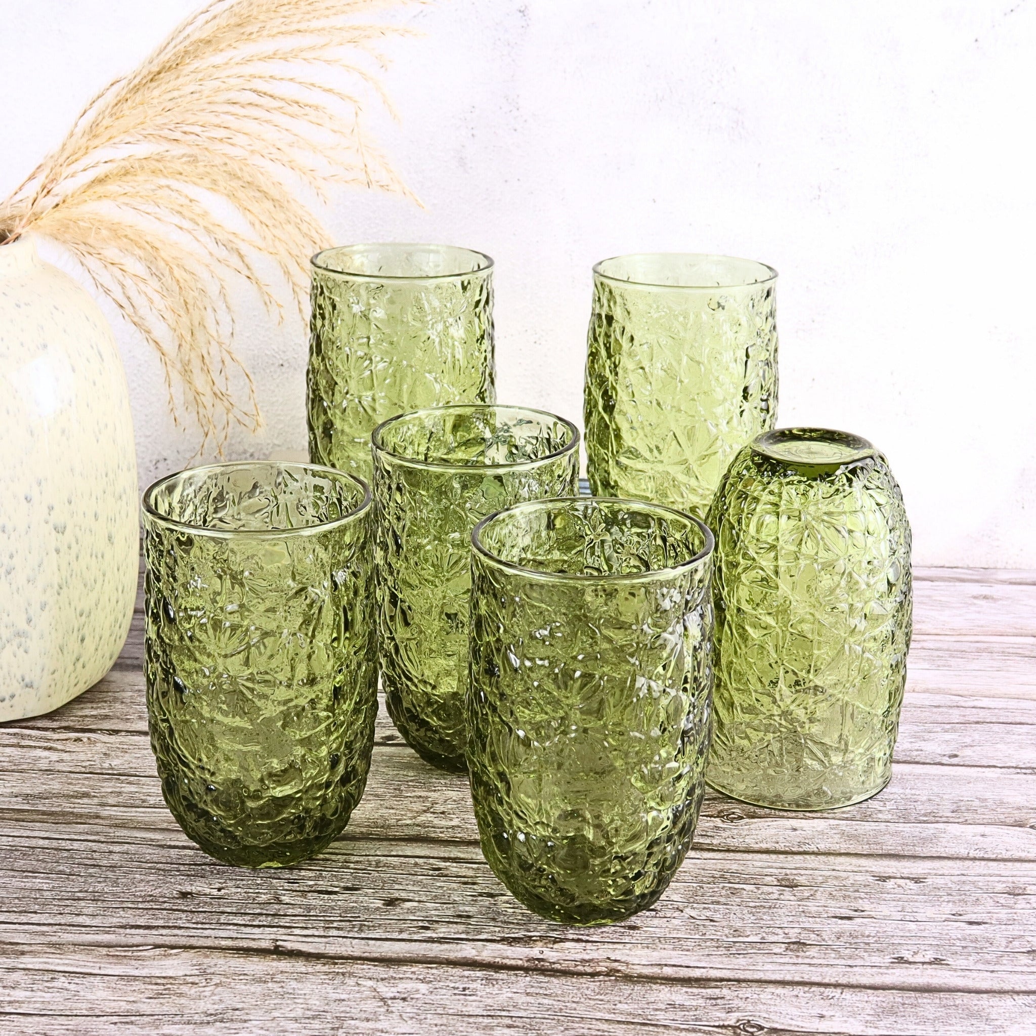 Set of green textured glass tumblers on a wooden surface with a white background