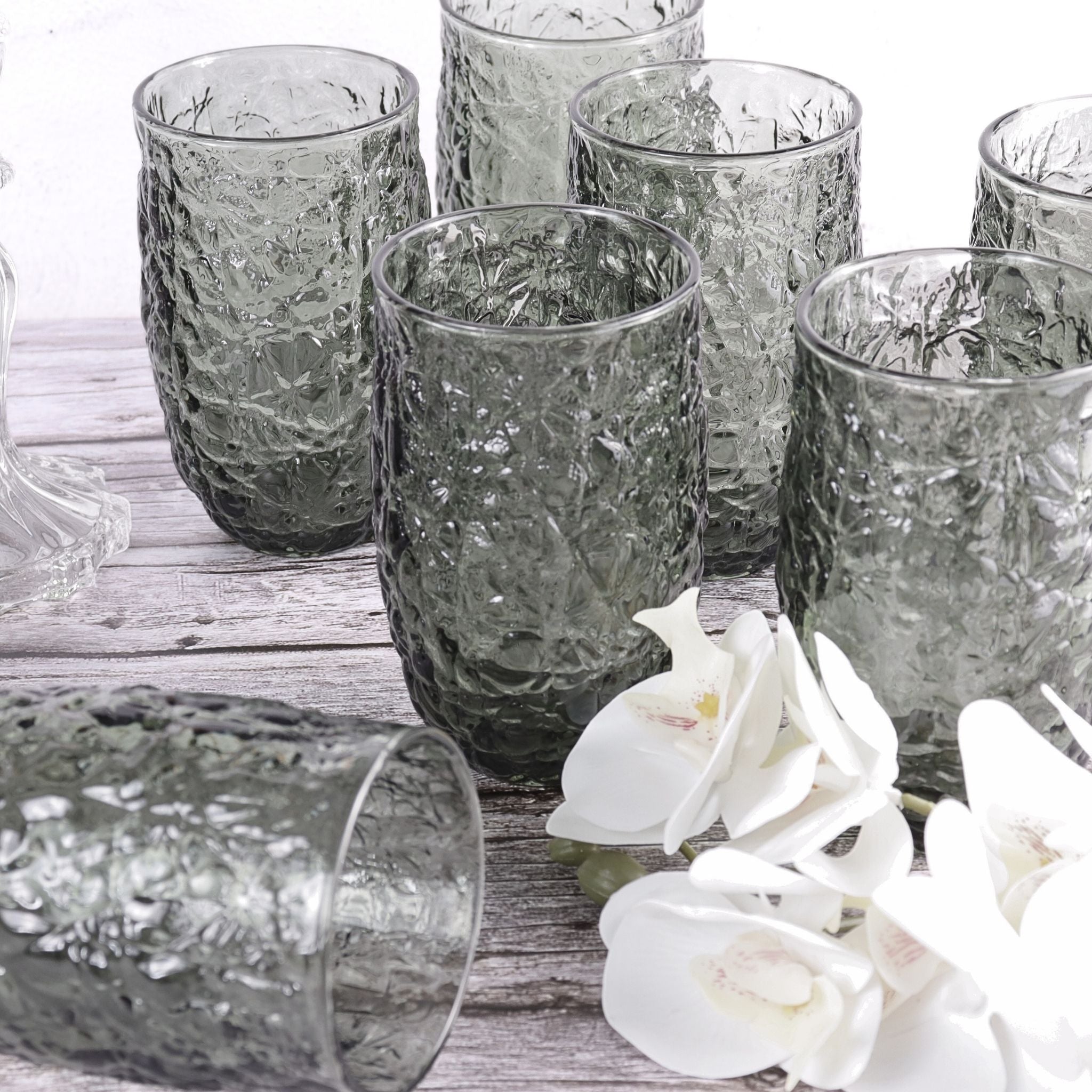 Set of textured glass tumblers on a wooden surface with white flowers.