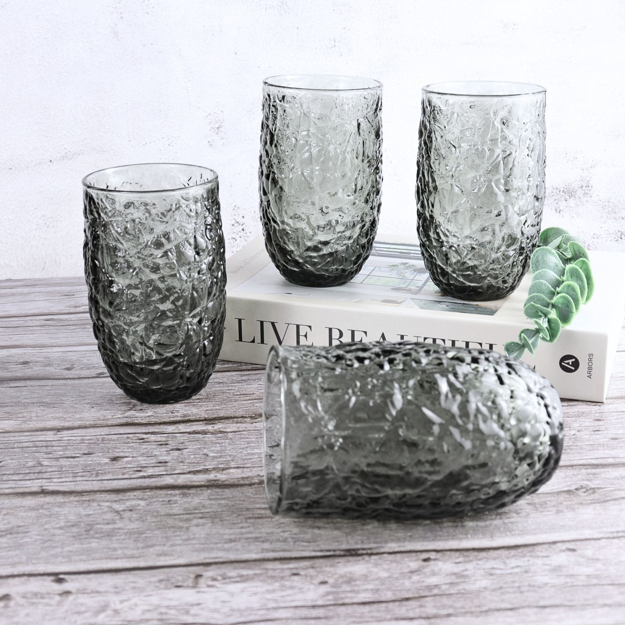 Set of textured glass tumblers on a wooden surface with a magazine in the background.