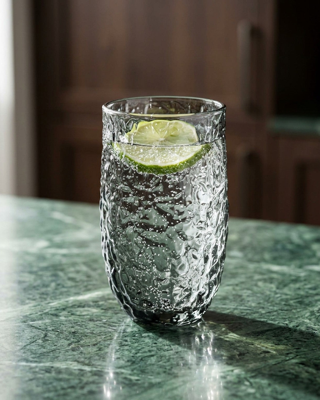 Set of textured gray glass tumblers on a wooden surface with a candle and book in the background.