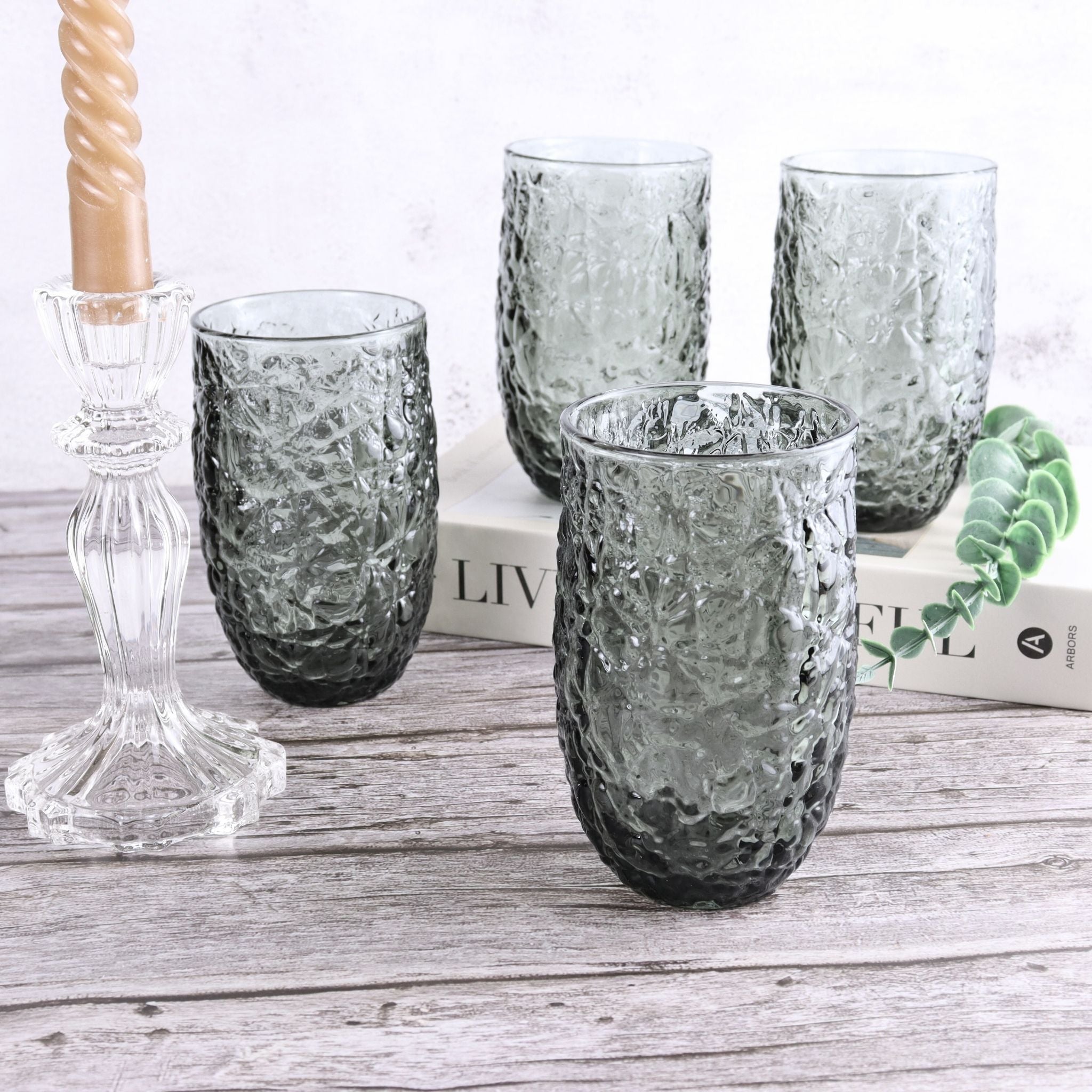 Set of textured gray glass tumblers on a wooden surface with a candle and book in the background.