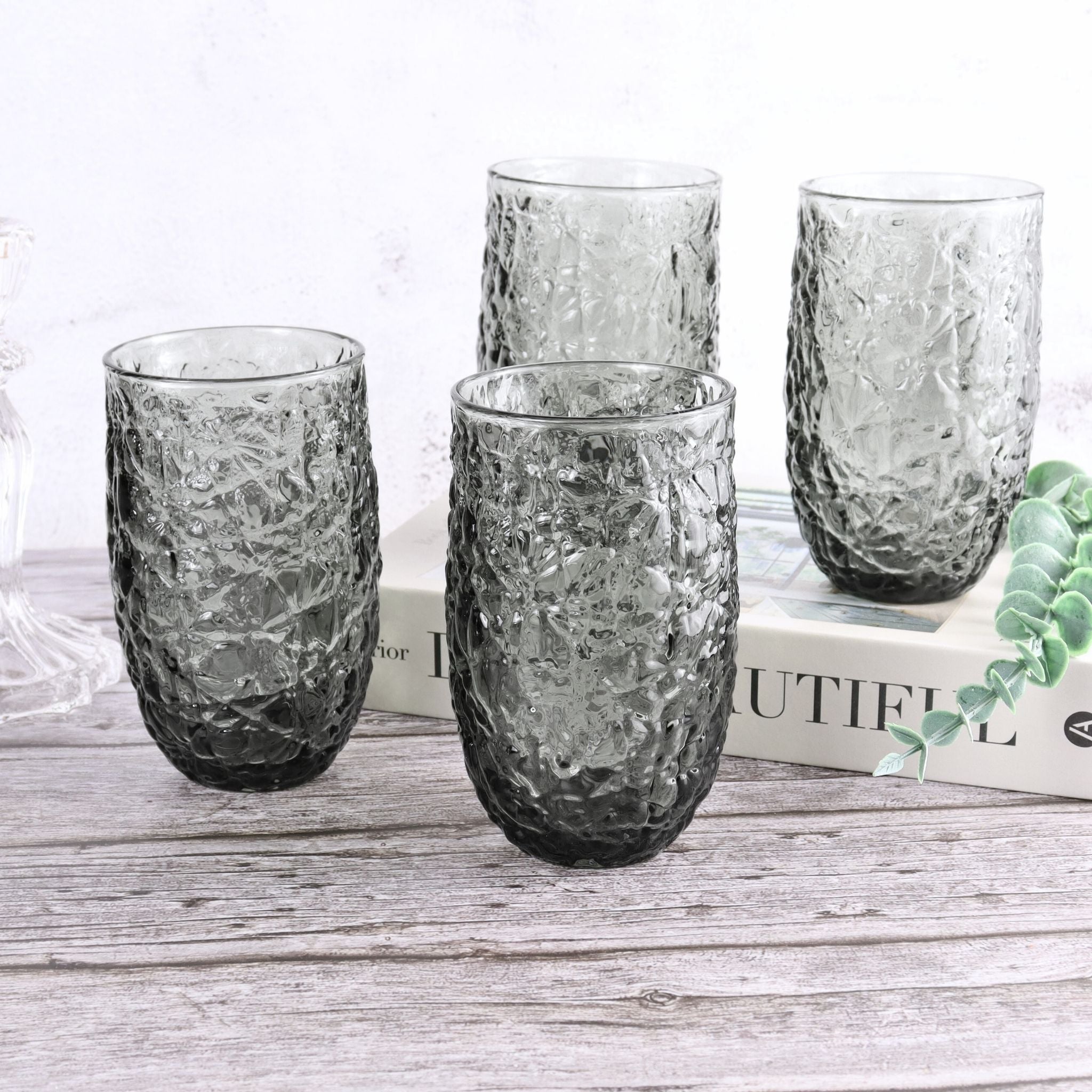 Set of four textured glass tumblers on a wooden surface with a magazine underneath.