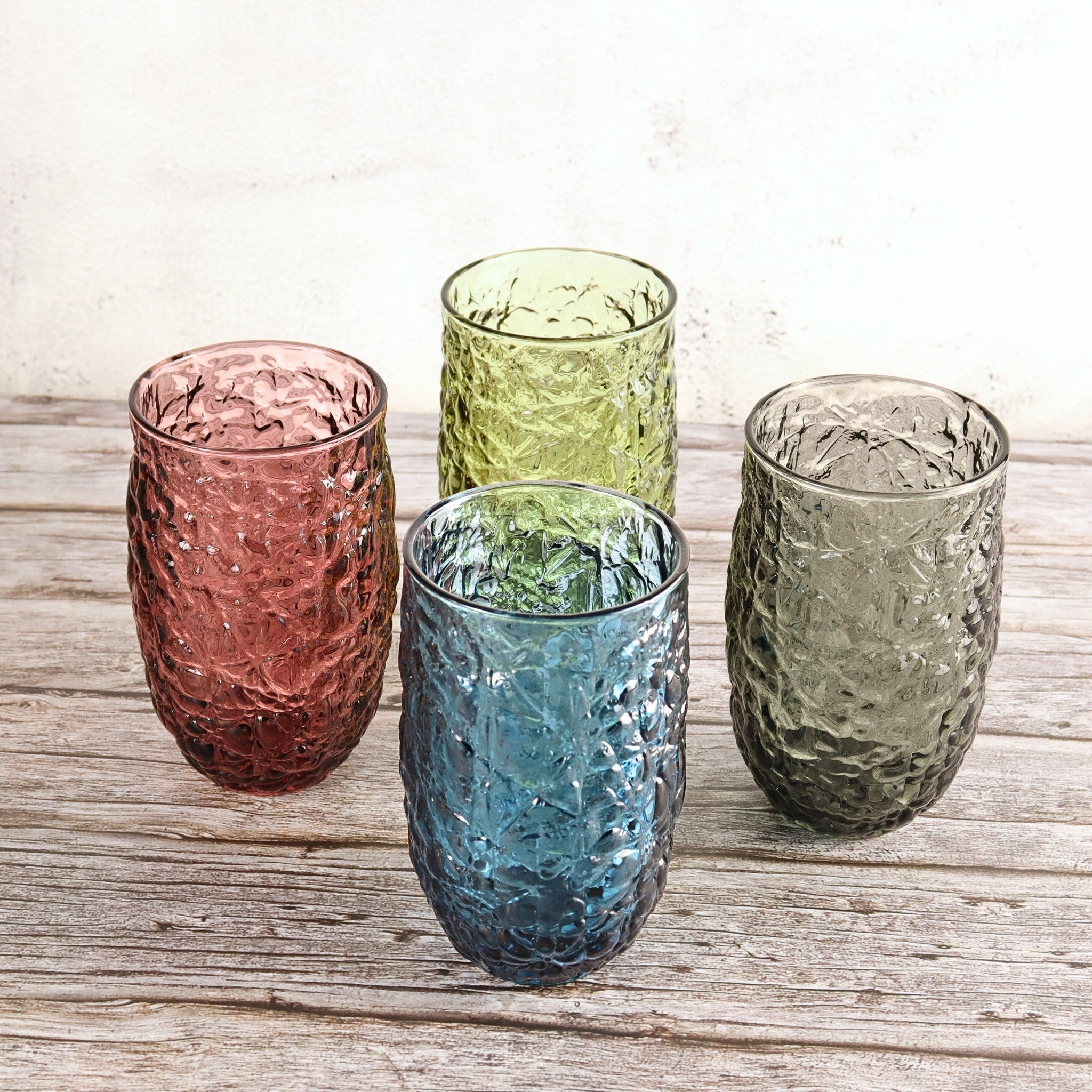 Four textured glass tumblers in pink, green, blue, and gray on a wooden surface.