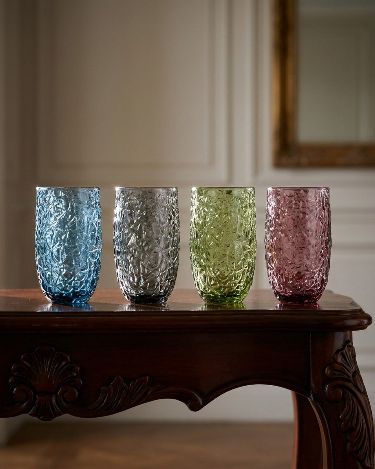 Four textured glass tumblers in different colors on a wooden surface with a light background.