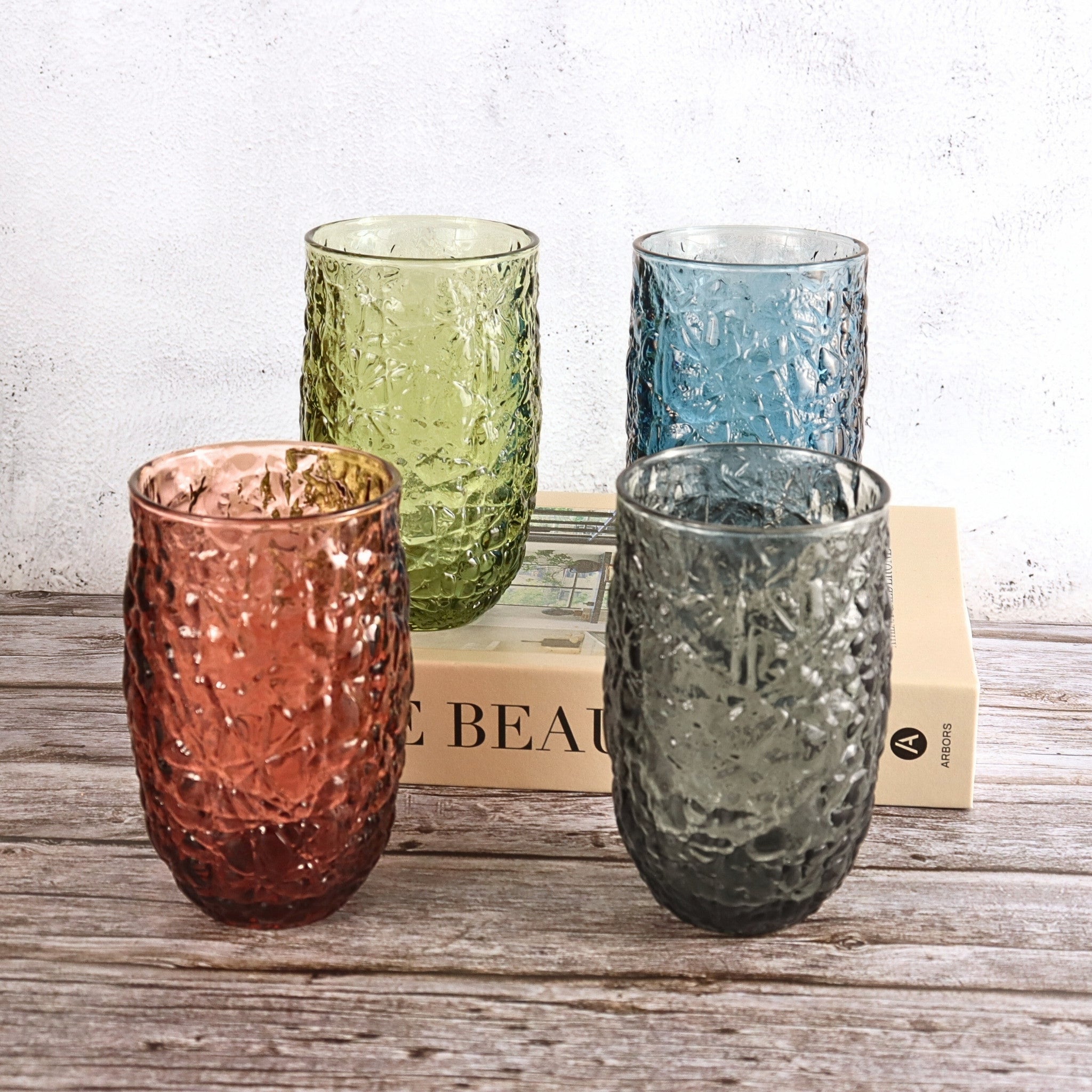 Four textured glass tumblers in different colors on a wooden surface with a light background.
