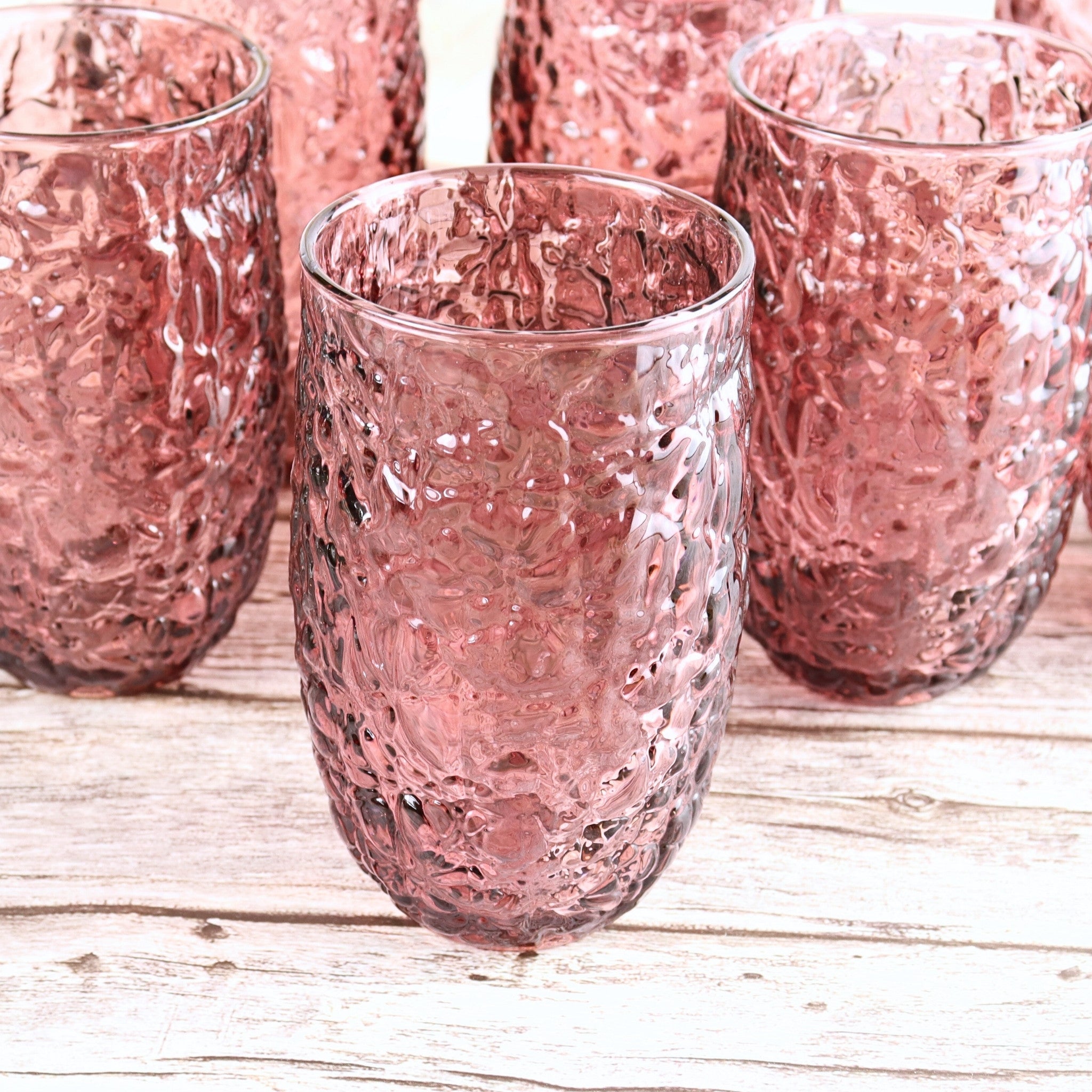 Set of pink textured glass tumblers on a wooden surface