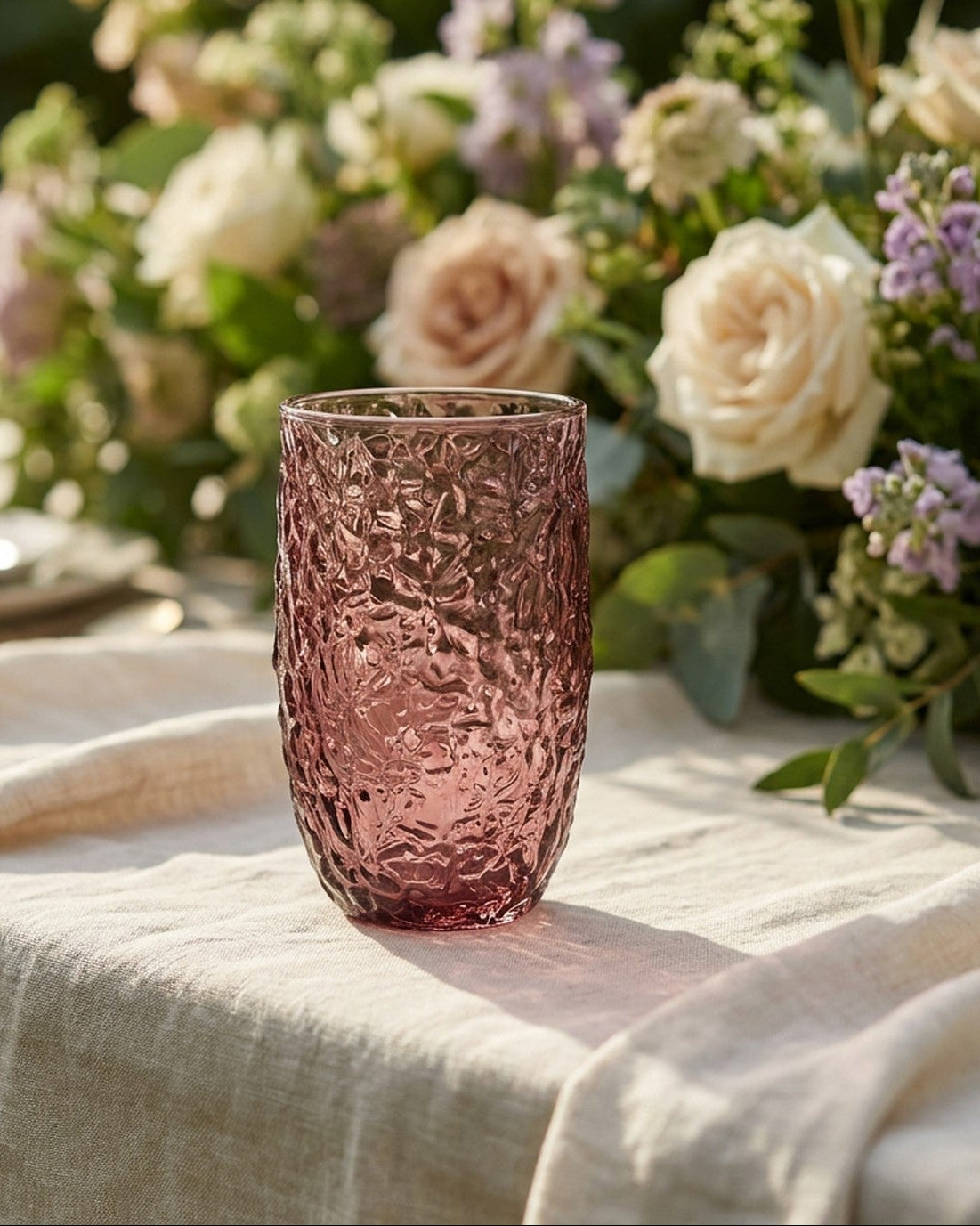 Two pink textured glass tumblers on a wooden surface with greenery.