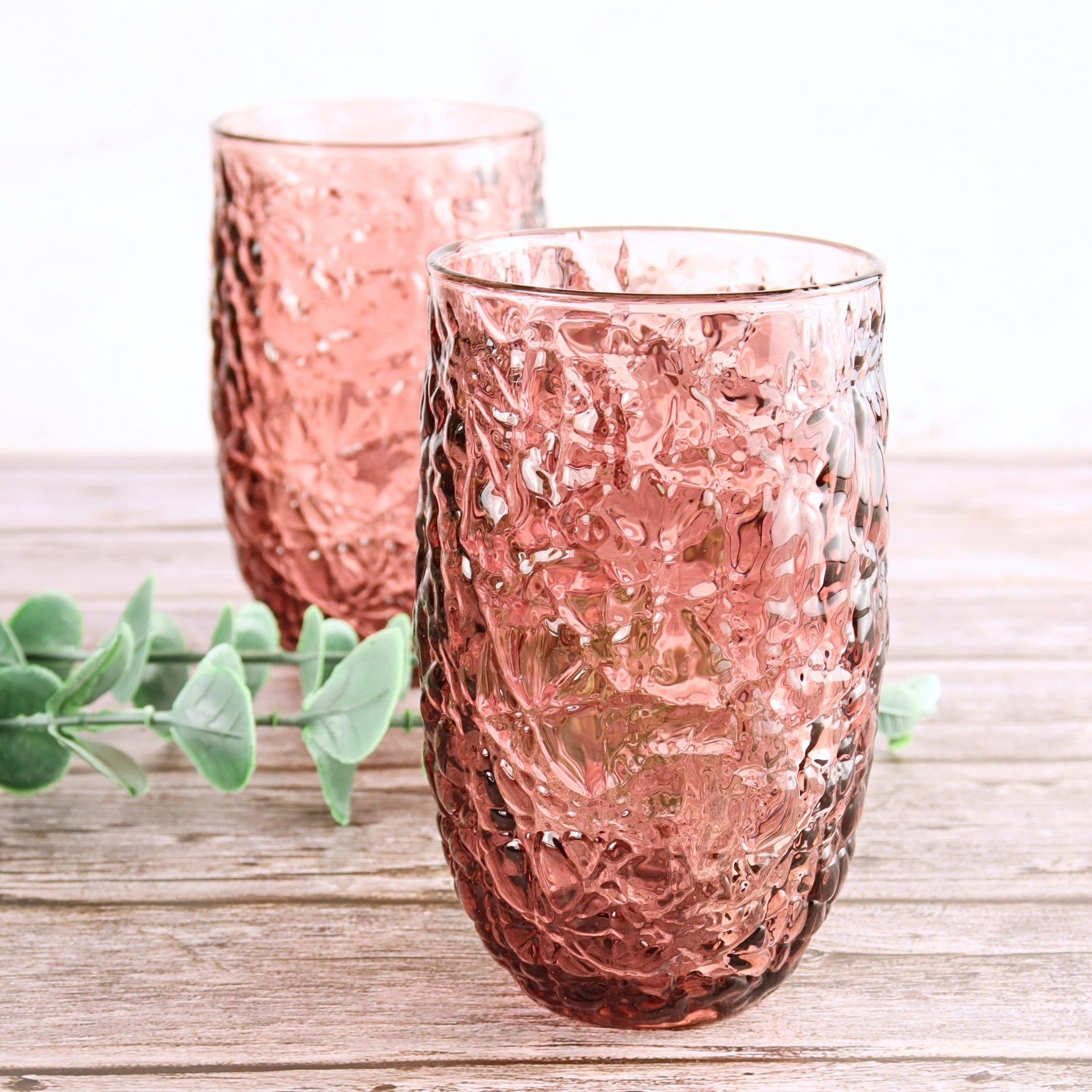 Two pink textured glass tumblers on a wooden surface with greenery.