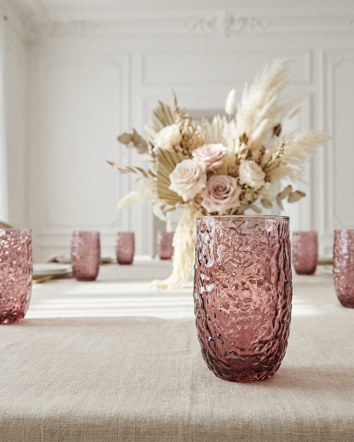 Two pink textured glass tumblers on a wooden surface with a light background