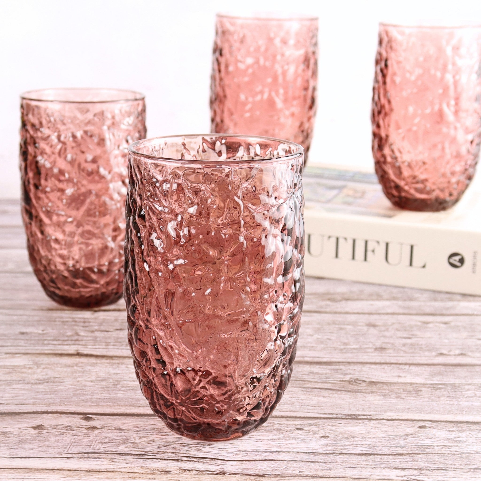 Set of pink textured glass tumblers on a wooden surface with a blurred book in the background.
