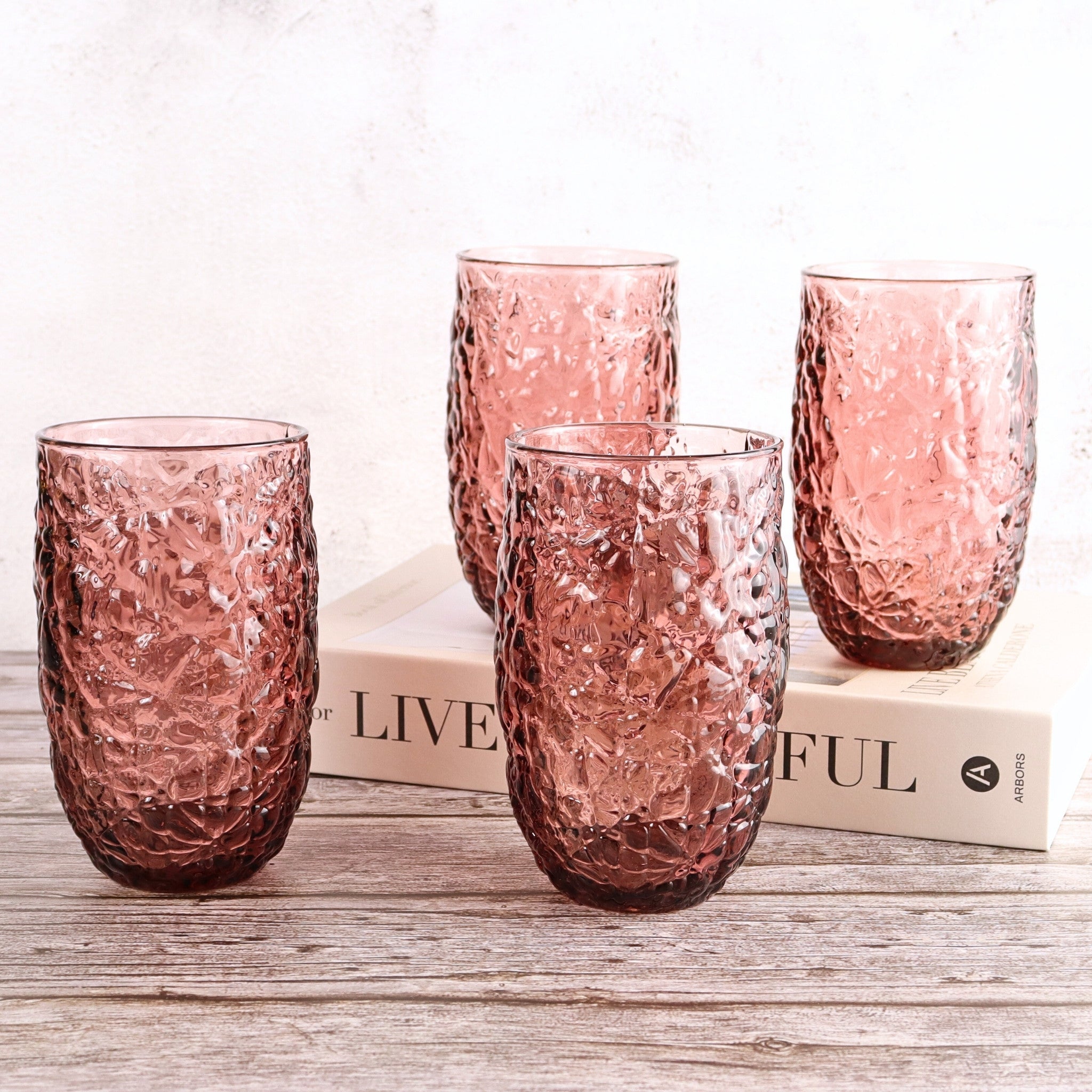 Set of four pink textured glass tumblers on a wooden surface with a blurred background.