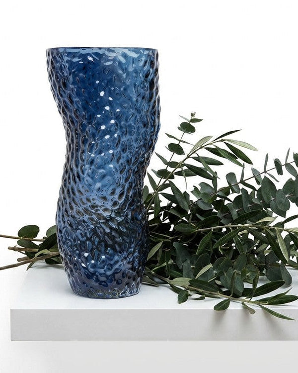 Blue textured vase with white flowers on a marble surface with a book in the background